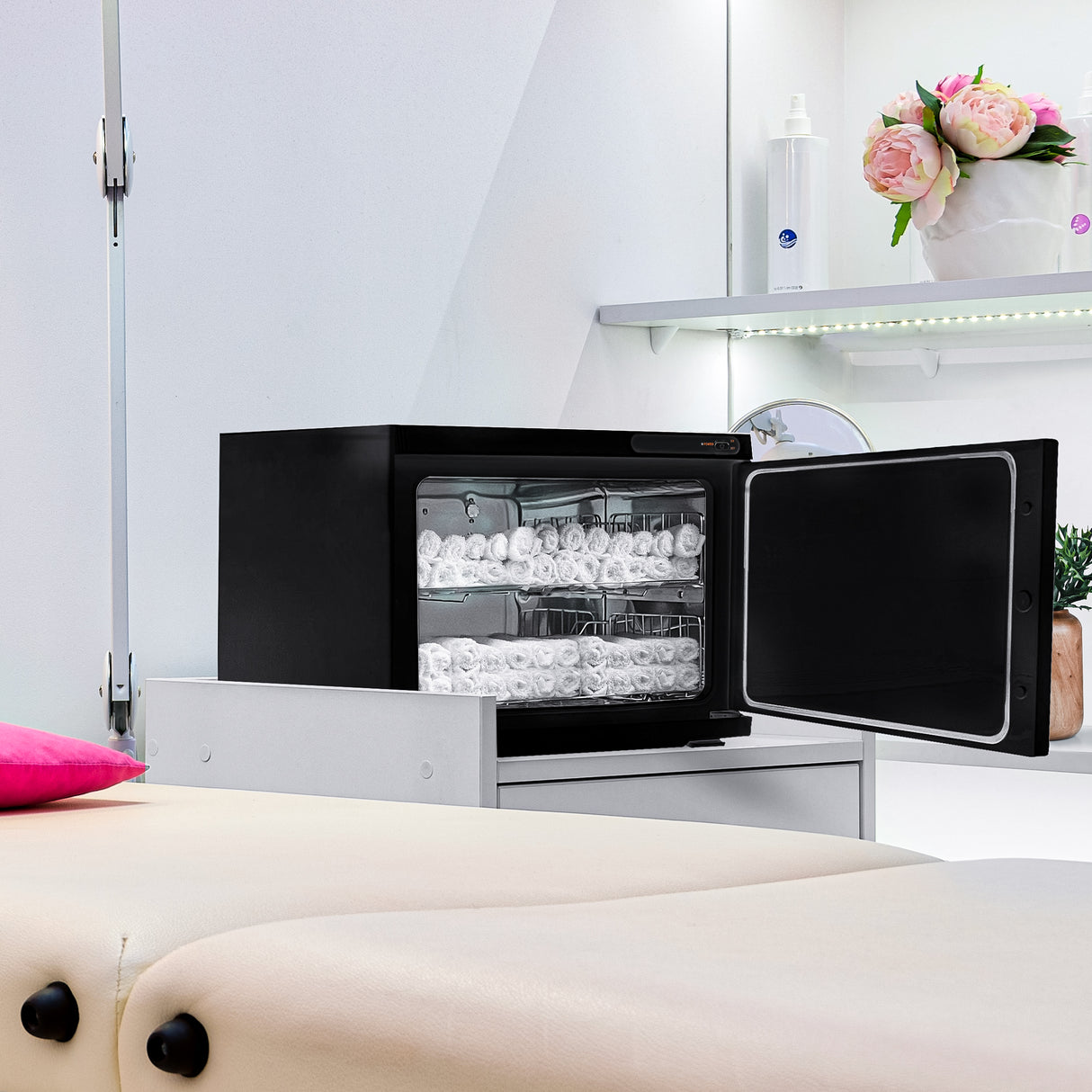 Chauffe-serviettes noir élégant de 23 L, avec porte vitrée, rempli de serviettes blanches, placé sur un meuble moderne dans un espace de soin
