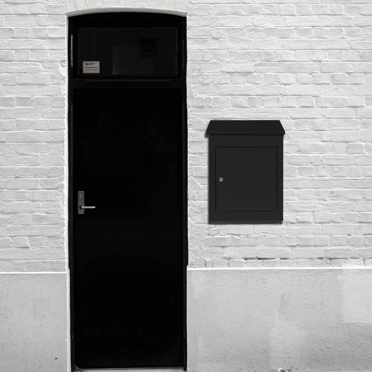 Boîte à colis anti-vol noire, design moderne, fixée sur un mur blanc, avec une texture lisse et un aspect élégant, idéale pour la sécurité des livraisons