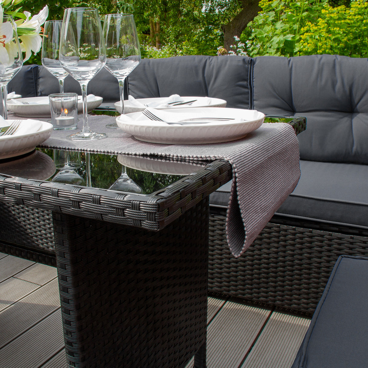 Salon de jardin en rotin noir pour 9 personnes, avec coussins gris, table en verre, assiettes blanches et verres à vin élégants