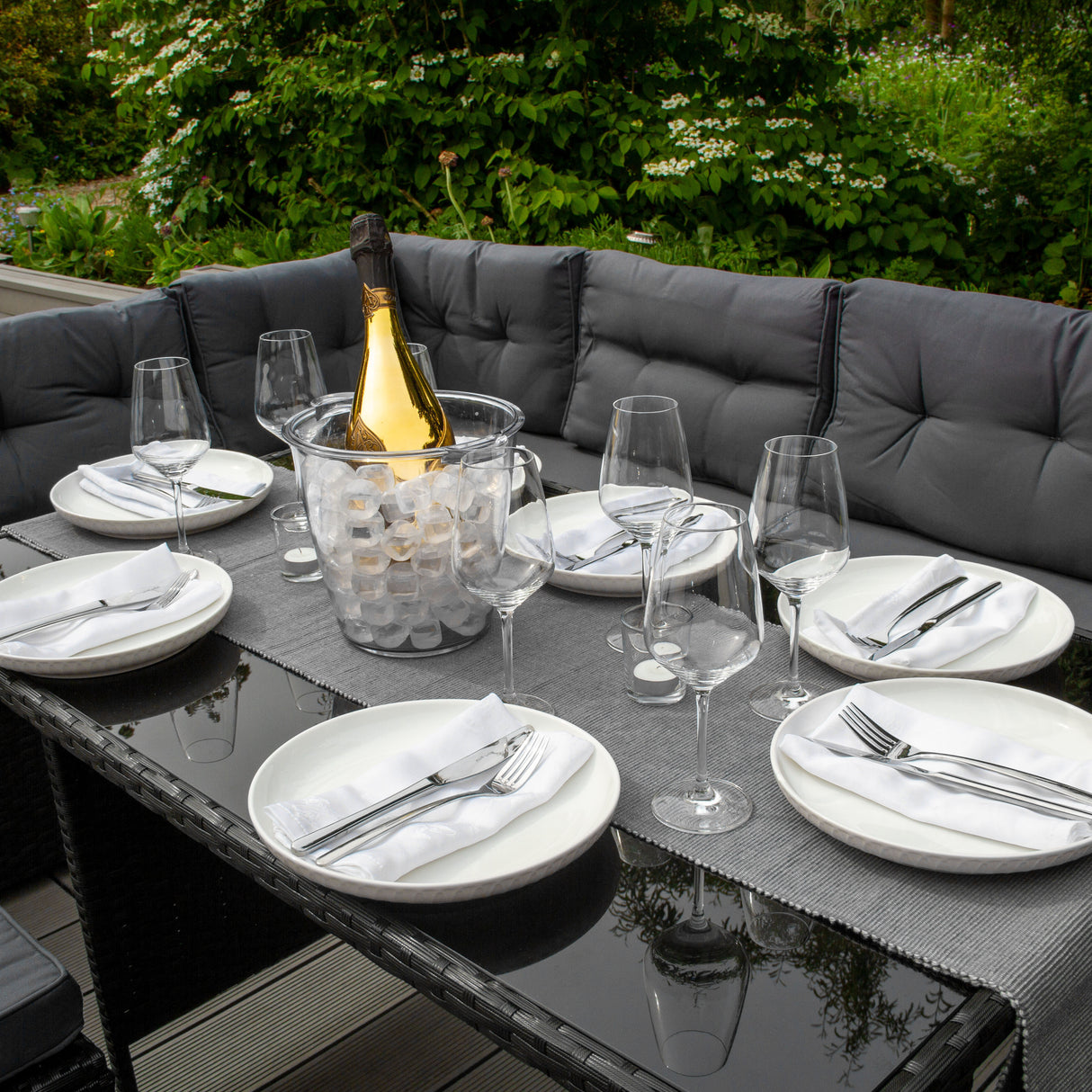 Salon de jardin en rotin noir pour 9 personnes, avec une table en verre, assiettes blanches, verres élégants et bouteille de champagne sur glace