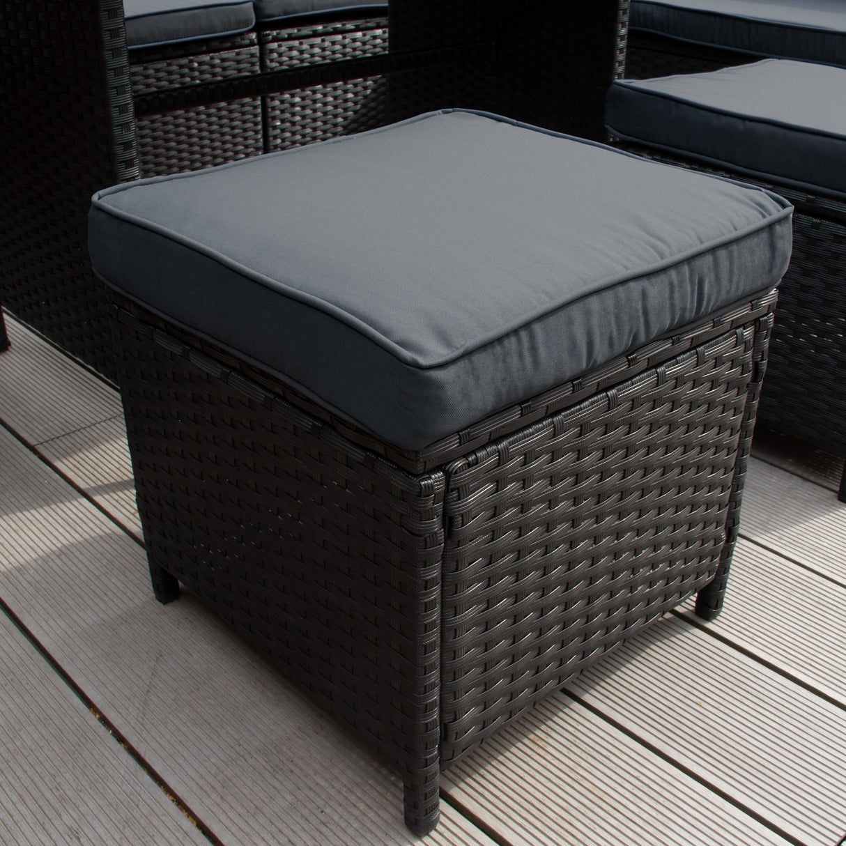 Coussin noir sur un pouf en rotin tressé, texture élégante, idéal pour un salon de jardin accueillant jusqu'à neuf personnes