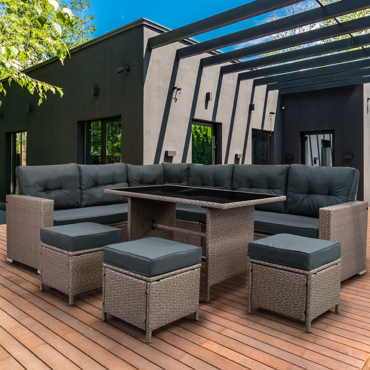 Salon de jardin en rotin gris pour 9 personnes, avec coussins noirs, table centrale en verre, sur une terrasse en bois