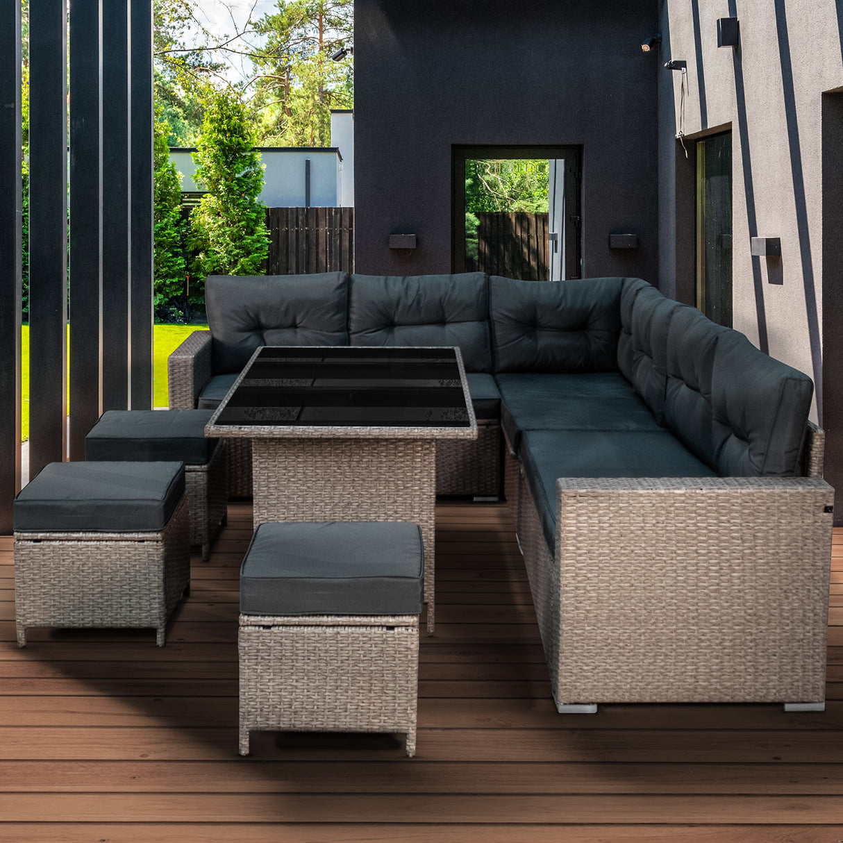 Salon de jardin en rotin gris pour 9 personnes, avec des coussins sombres et une table en verre, sur une terrasse en bois