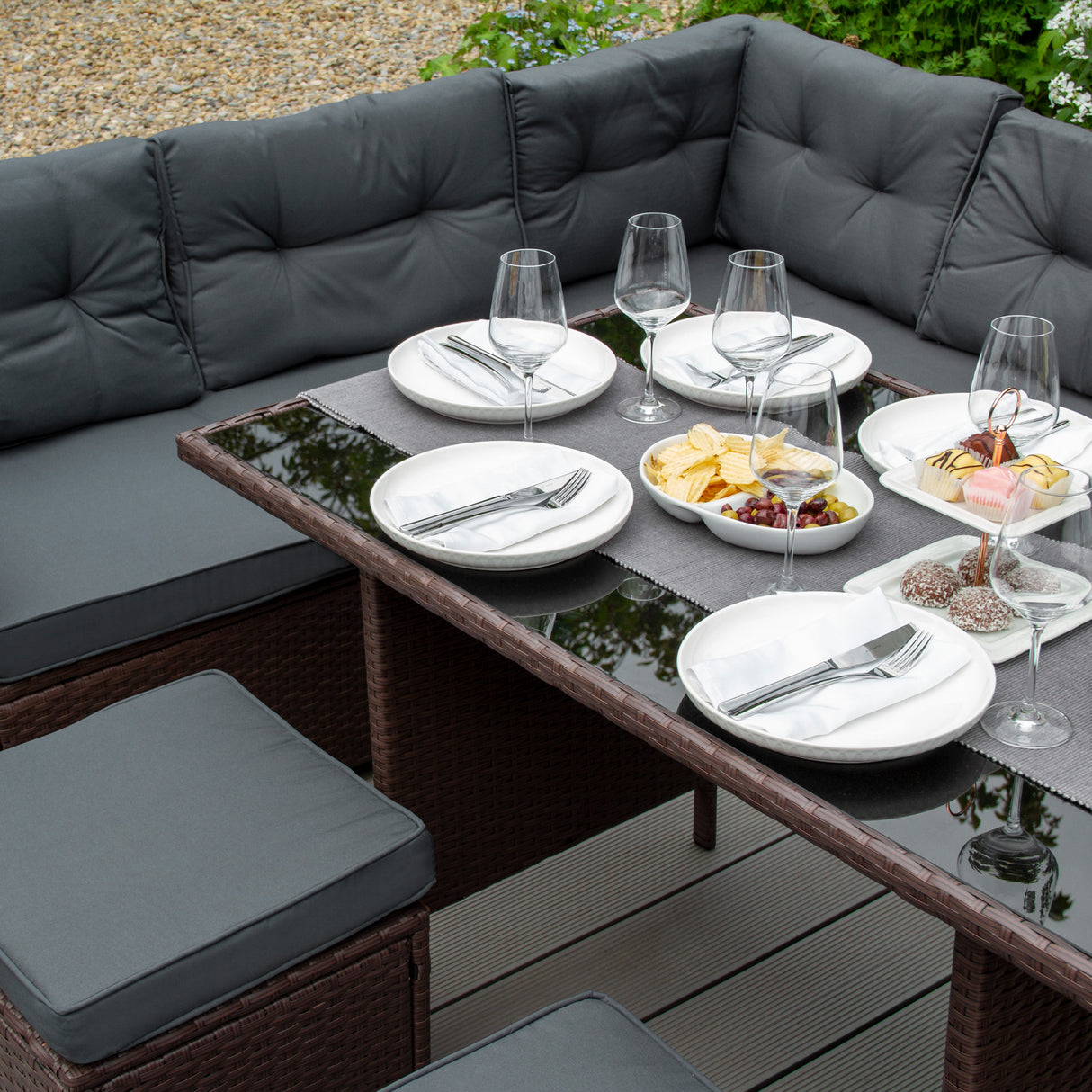Salon de jardin en rotin marron pour 9 personnes, avec coussins gris, table en verre, assiettes et verres élégants disposés pour un repas convivial