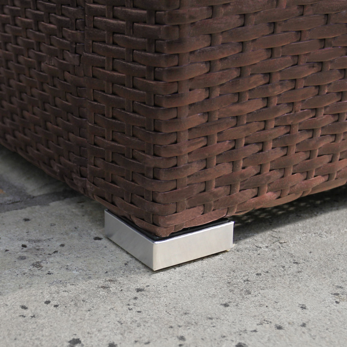 Détail du coin d'un salon de jardin en rotin marron, mettant en avant la texture tissée et le support en métal argenté