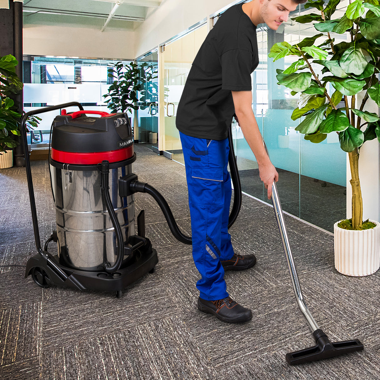 Aspirateur industriel MAXBLAST de 80 L avec accessoires, utilisé par un homme en tenue de travail dans un bureau moderne, plantes en arrière-plan