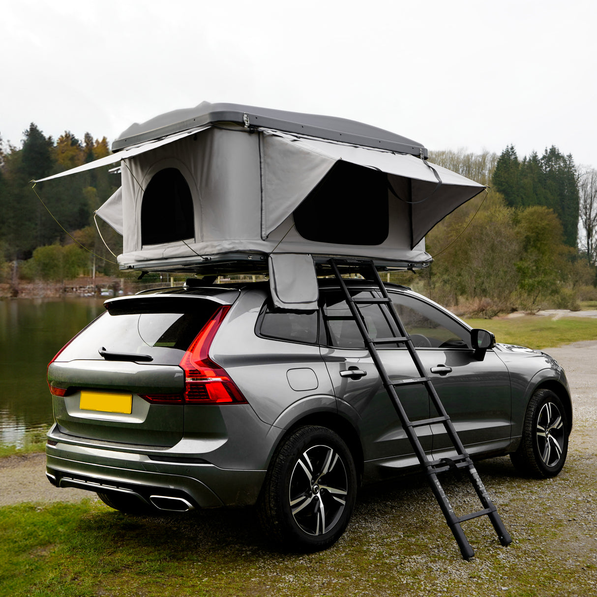 Tente de toit grise montée sur un véhicule, avec des fenêtres ouvertes, échelle en aluminium et un paysage naturel en arrière-plan