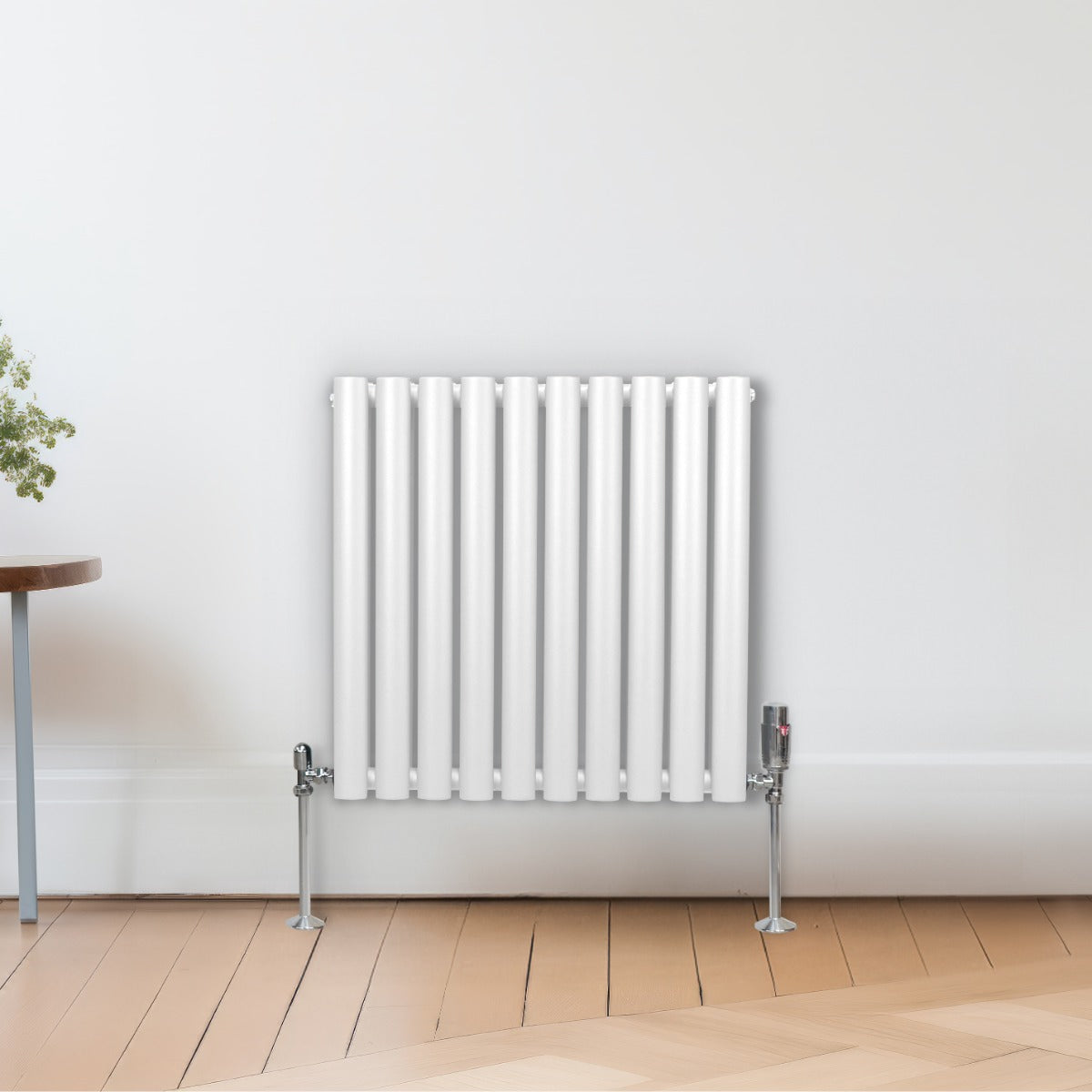 Radiateur à colonnes ovales blanc, 2 panneaux, 600 x 600 mm, installé sur un mur avec un sol en bois clair et une plante à côté