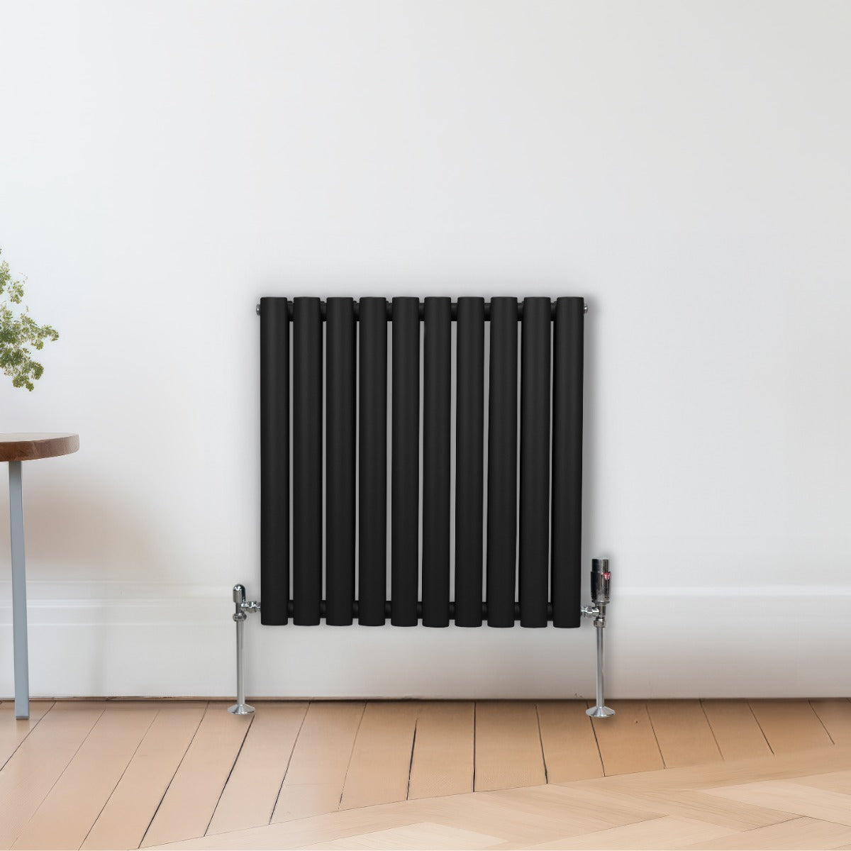 Radiateur à colonnes ovales noir, 2 panneaux, 600 x 600 mm, avec finition lisse et pieds en métal, installé sur un mur blanc
