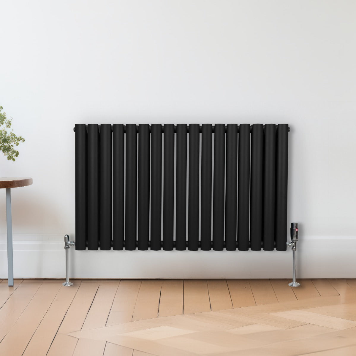 Radiateur à colonnes ovales noir, 2 panneaux, 600 x 1020 mm, avec finition lisse et pieds en métal, installé contre un mur blanc