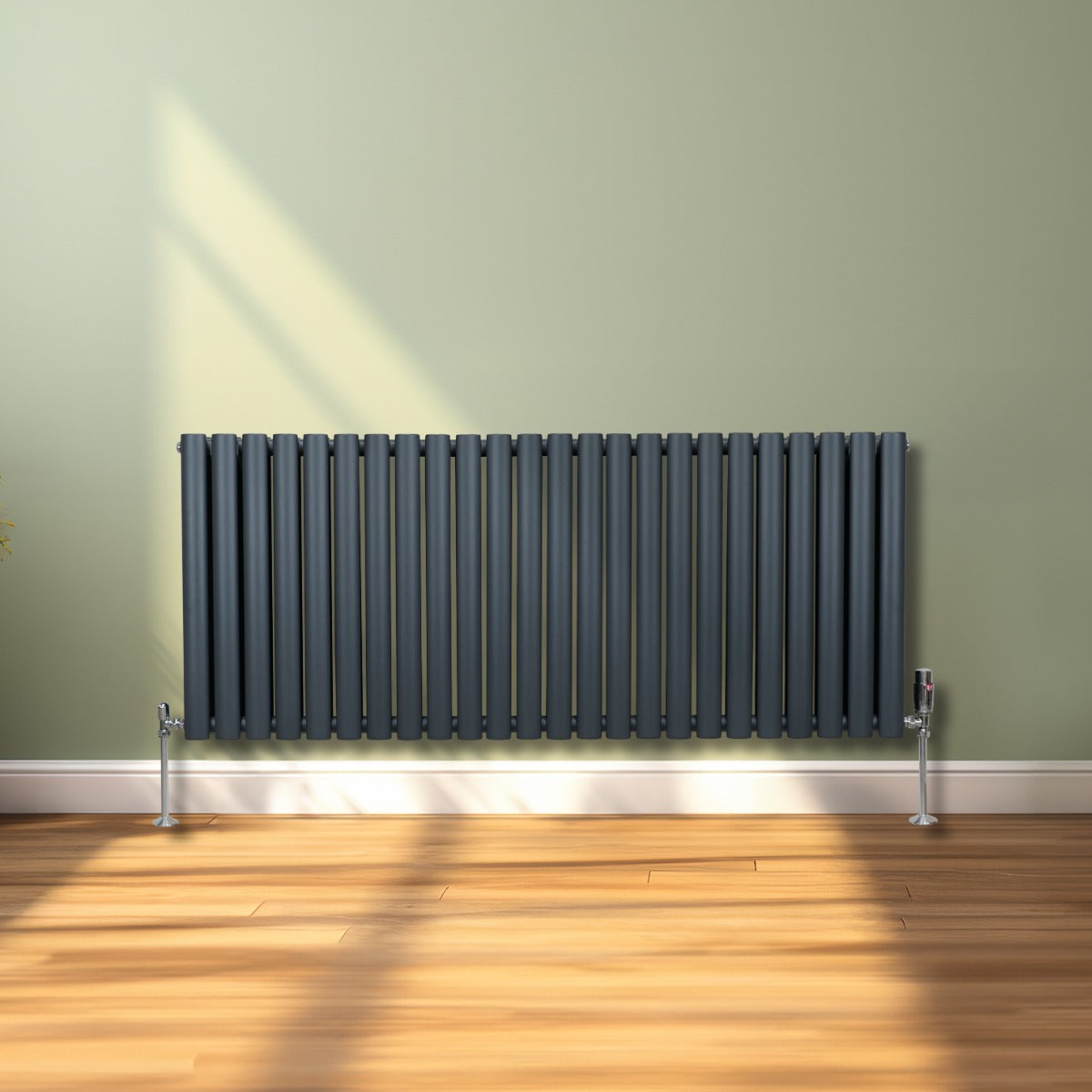 Radiateur à colonnes ovales gris anthracite, 2 panneaux, installé contre un mur, avec un sol en bois clair et lumière naturelle