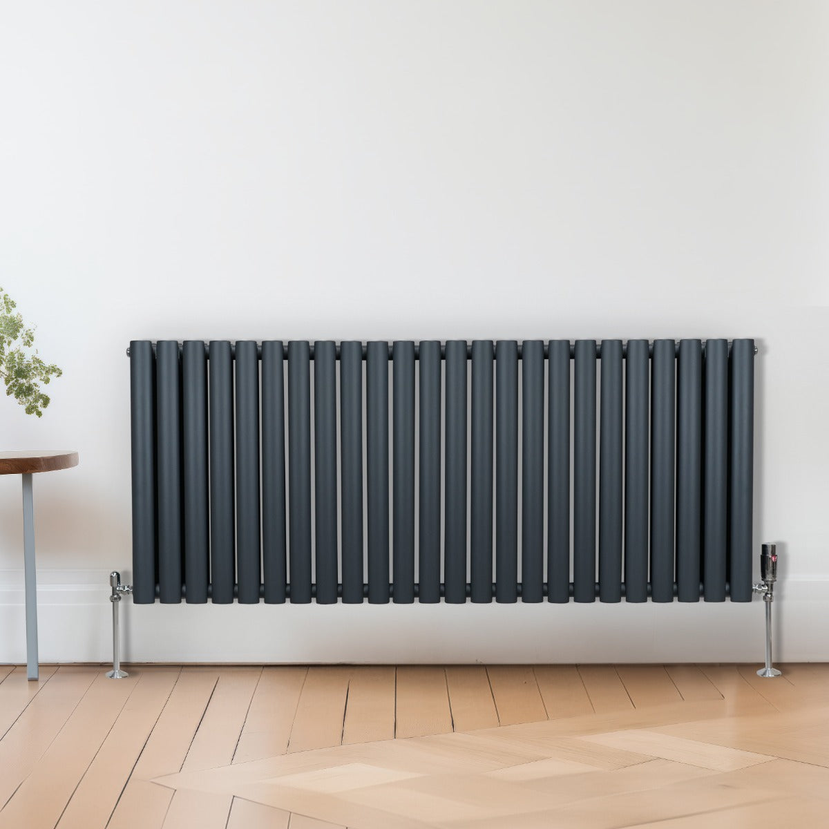 Radiateur à colonnes ovales gris anthracite, 2 panneaux, installé sur un mur, avec des pieds en métal et un sol en bois clair