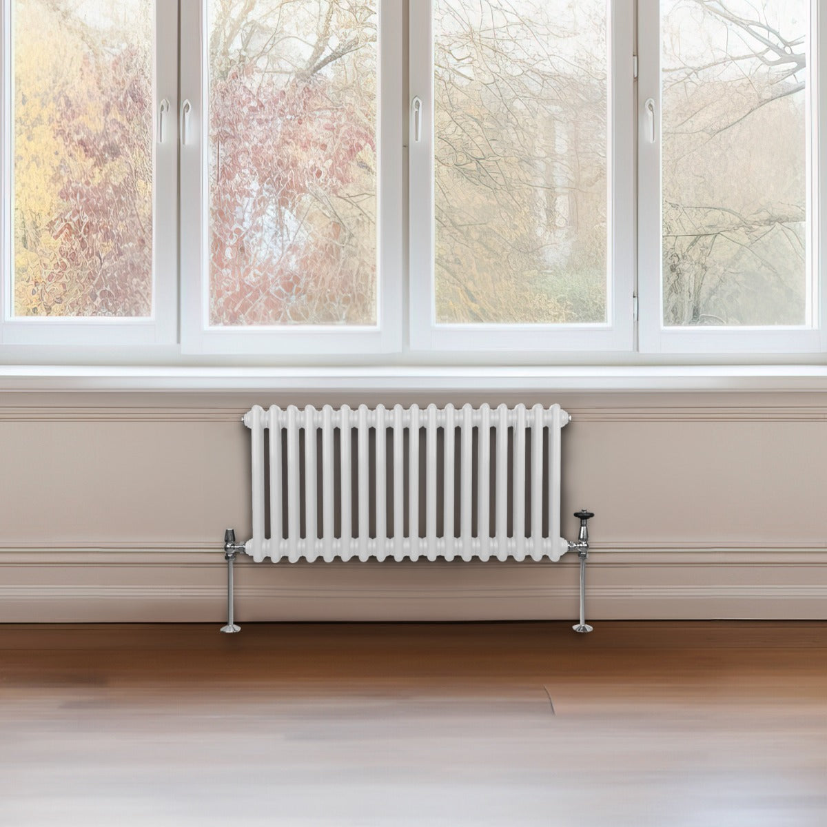Radiateur traditionnel à 2 colonnes, blanc, installé sous une fenêtre, avec des tuyaux en métal et un sol en bois clair