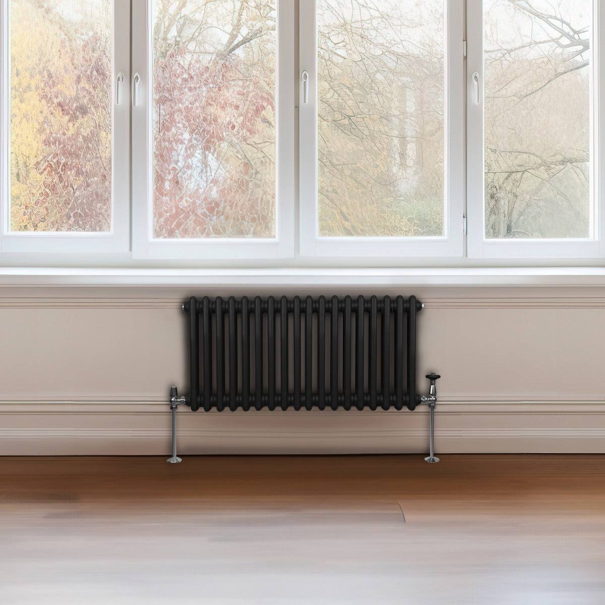 Radiateur traditionnel noir à deux colonnes, 300 x 832 mm, installé sous une fenêtre, avec un sol en bois clair et vue sur le jardin
