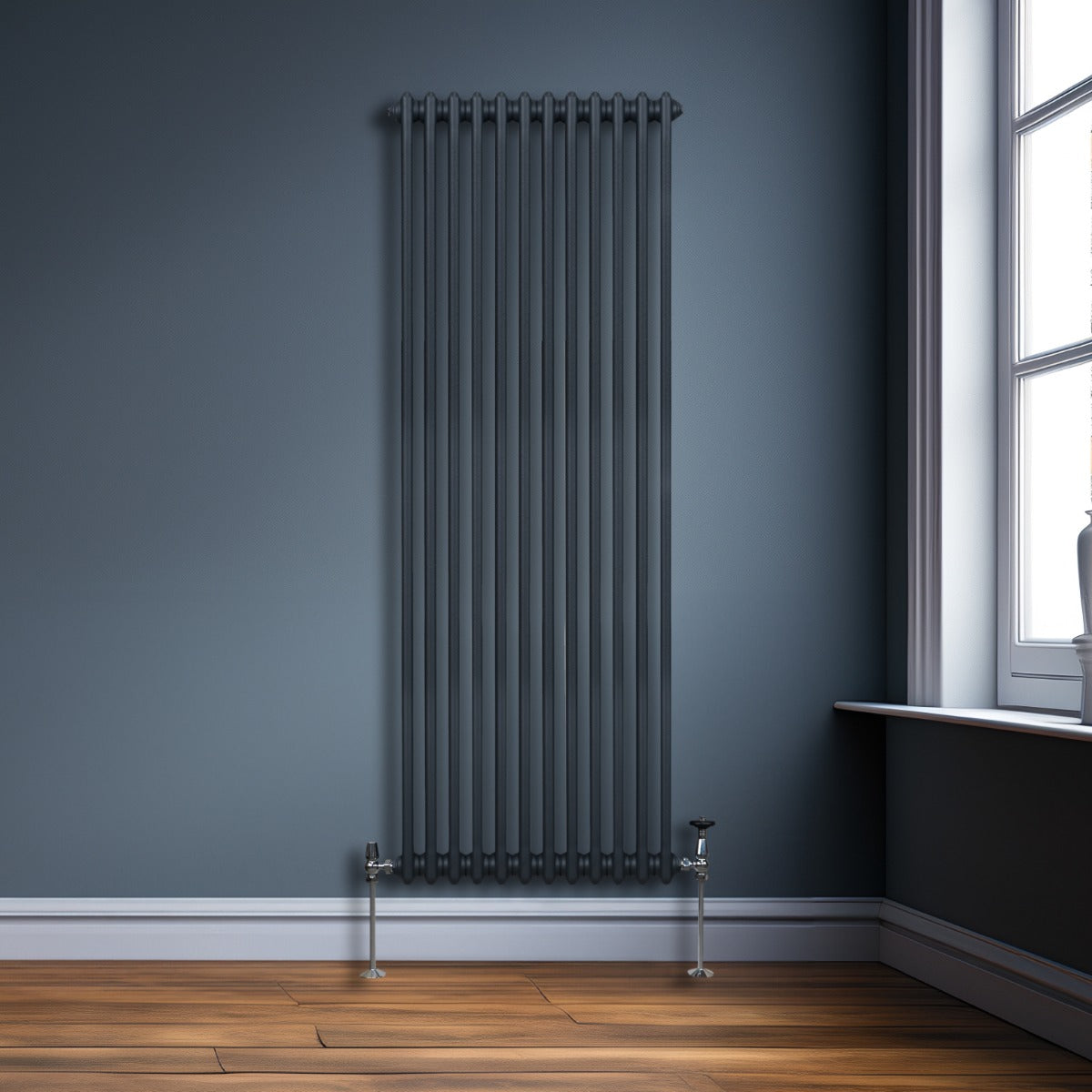 Radiateur traditionnel à deux colonnes gris anthracite, haut et étroit, installé contre un mur bleu, avec un sol en bois chaleureux