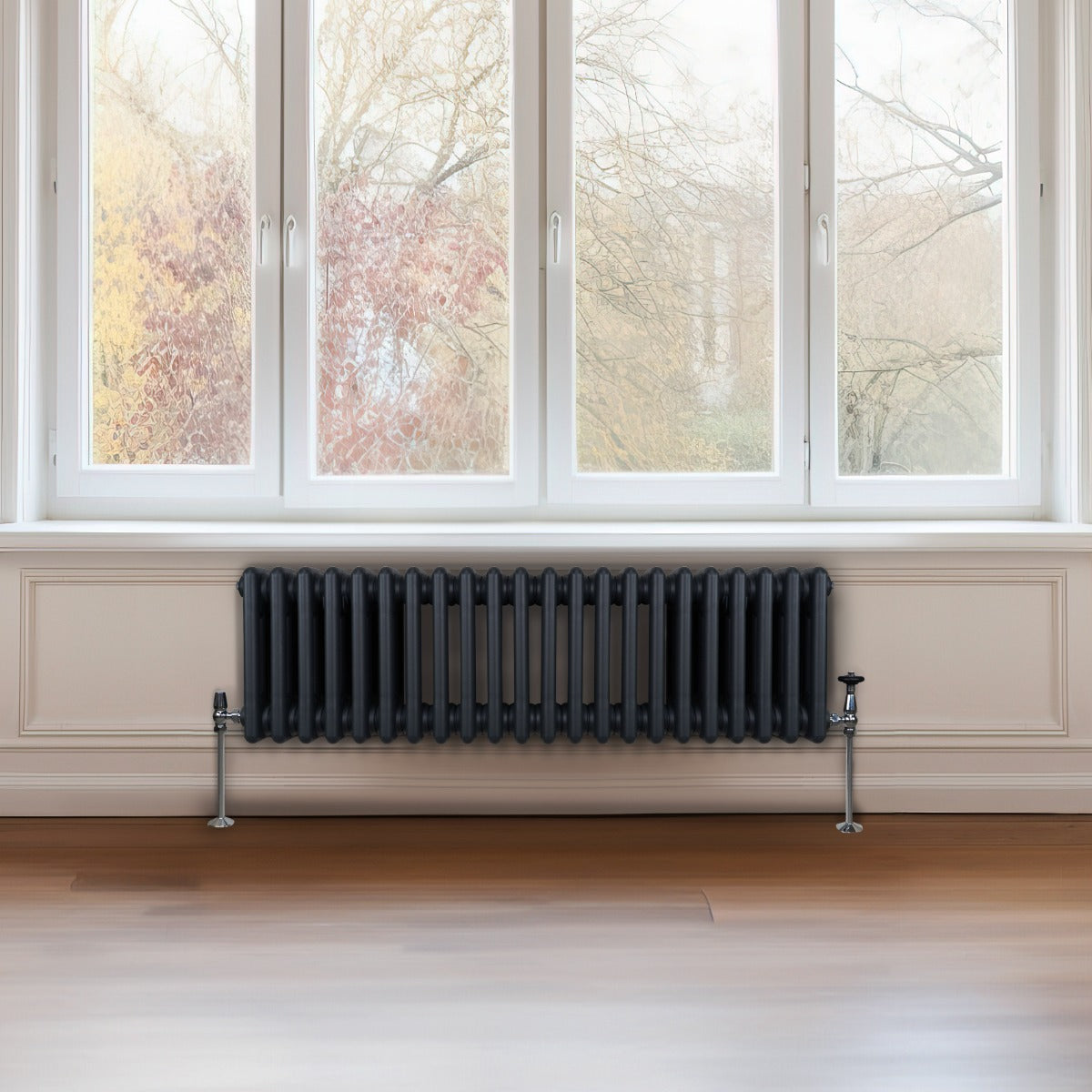 Radiateur traditionnel à 3 colonnes gris anthracite, installé sous une fenêtre, avec des tuyaux en métal et un sol en bois clair