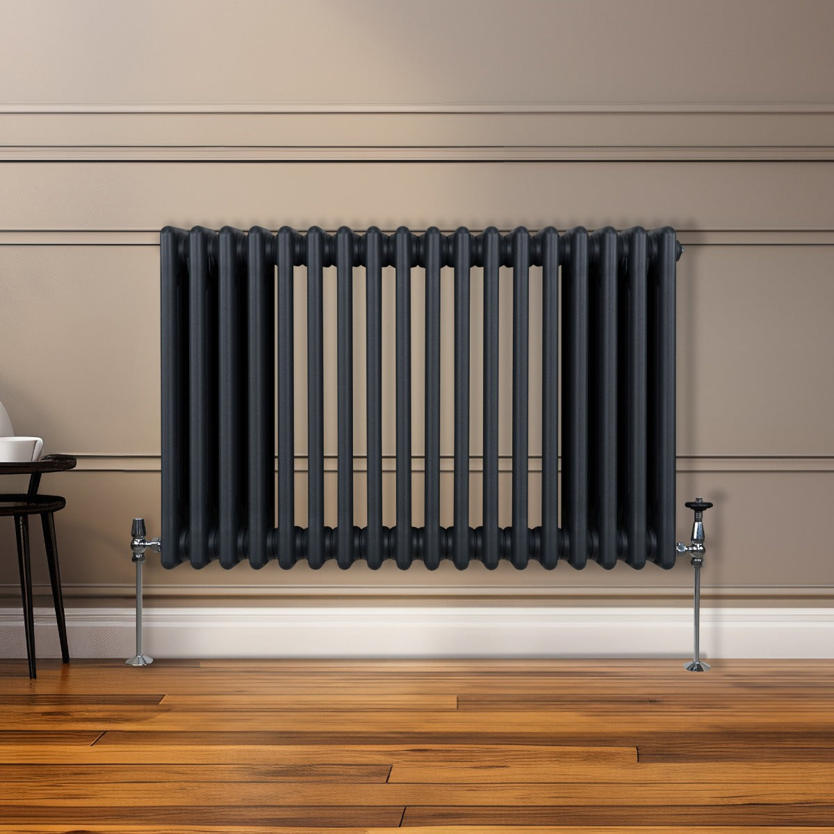 Radiateur traditionnel à 3 colonnes gris anthracite, installé sur un mur beige, avec des pieds en métal et un sol en bois chaleureux