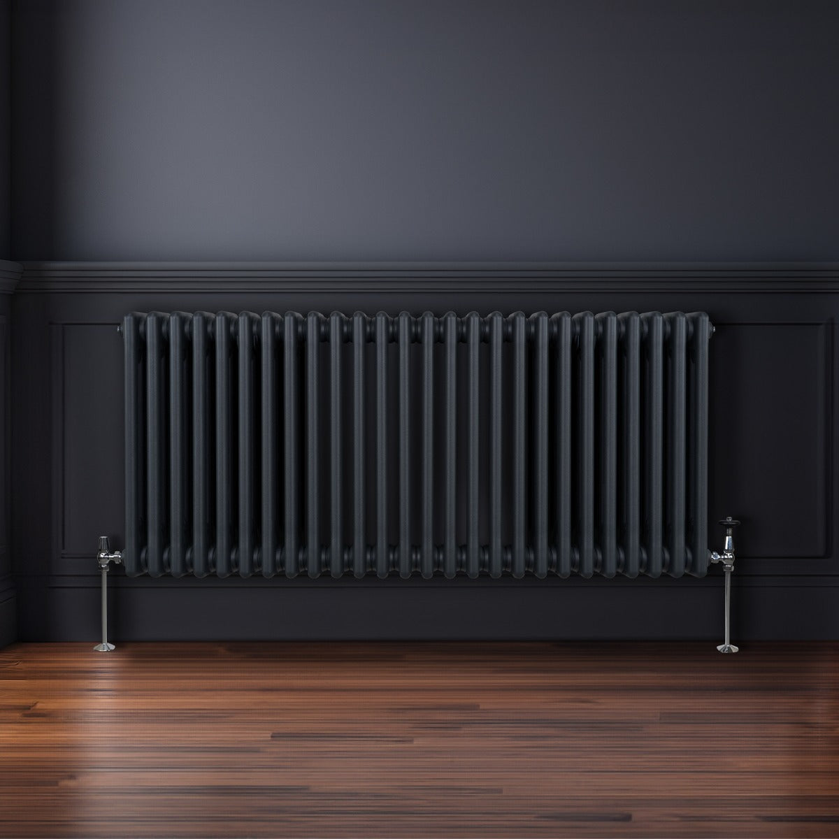 Radiateur traditionnel à 3 colonnes gris anthracite, installé sur un mur noir, avec des pieds en métal brillant et un sol en bois chaleureux