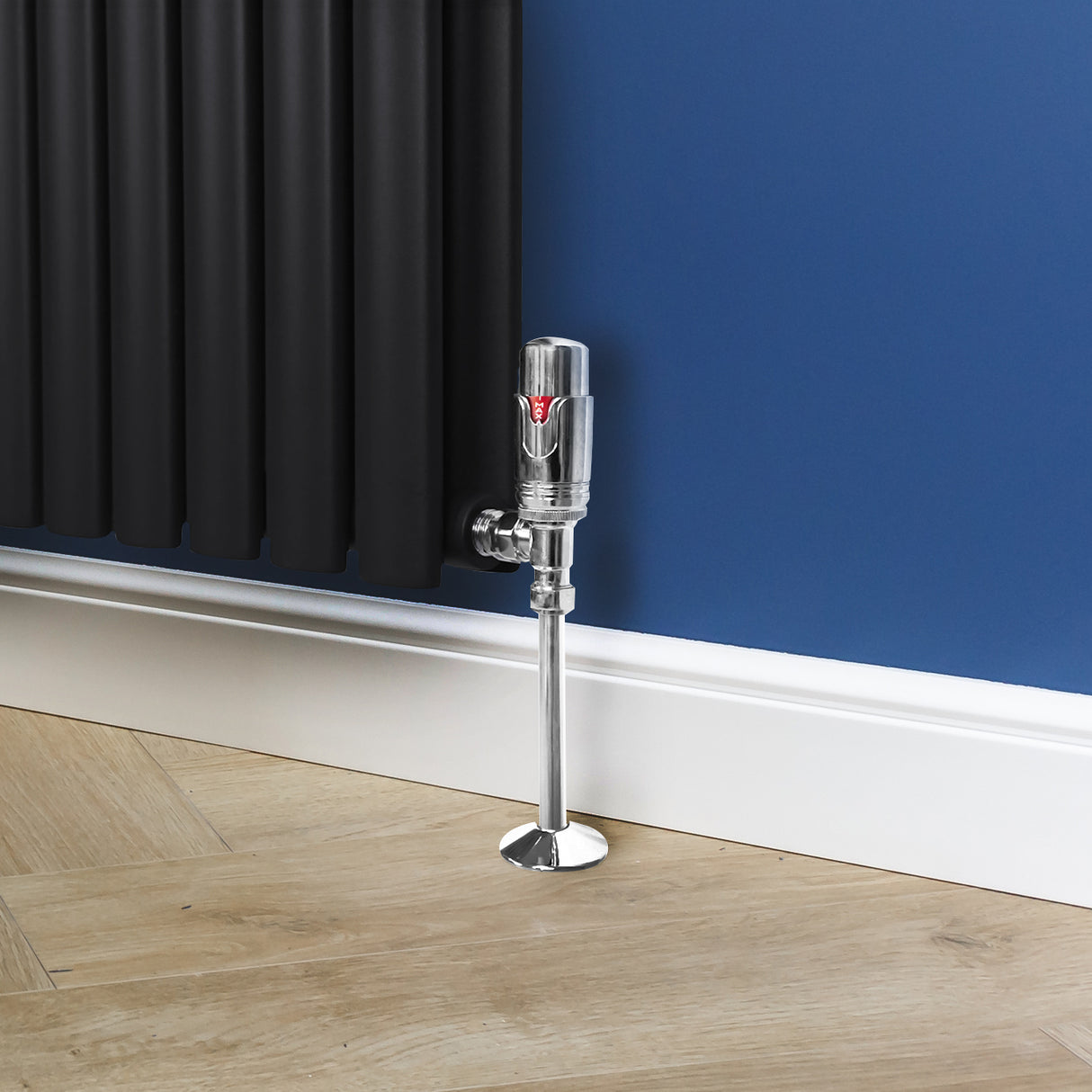 Vanne de radiateur thermostatique en laiton chromé, avec une finition brillante, positionnée près d'un radiateur noir sur un sol en bois clair