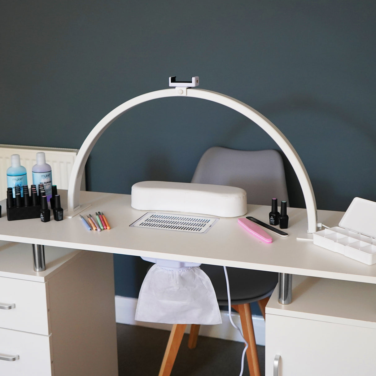 Lampe de manucure LED demi-lune blanche, design élégant, positionnée sur un bureau moderne avec divers outils de manucure colorés