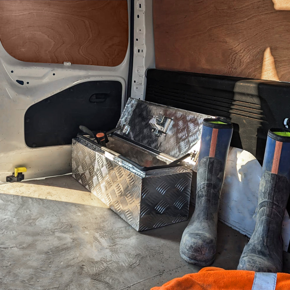 Caisse à outils en aluminium argenté, finition en relief, posée dans un fourgon avec des bottes en caoutchouc et un tissu orange à côté