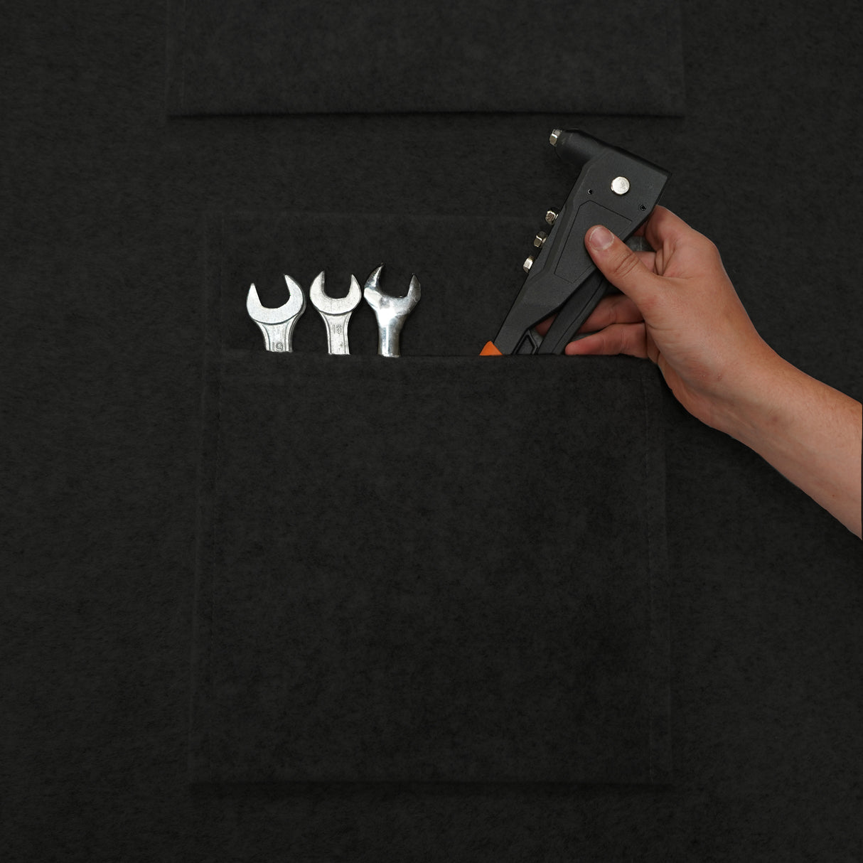 Poches de rangement noires en feutre, contenant des outils en métal, avec une main tenant un pistolet à agrafes en position d'utilisation