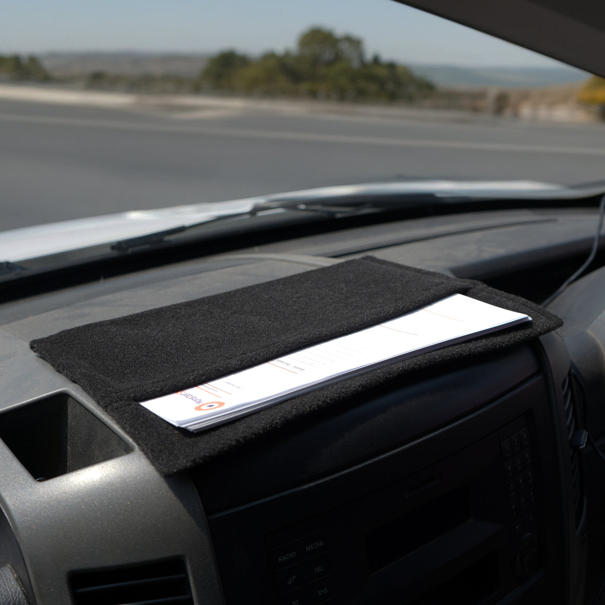 Poche de rangement noire en tissu doux, posée sur le tableau de bord d'une voiture, idéale pour organiser documents et accessoires