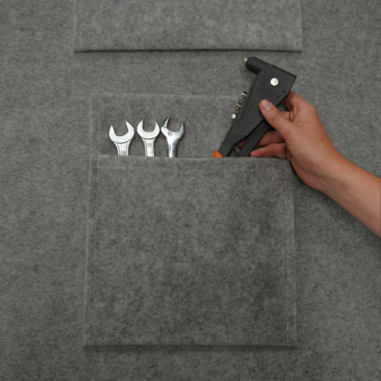 Poches de rangement en feutre gris clair, contenant des clés à molette et un pistolet à colle, offrant une texture douce et durable