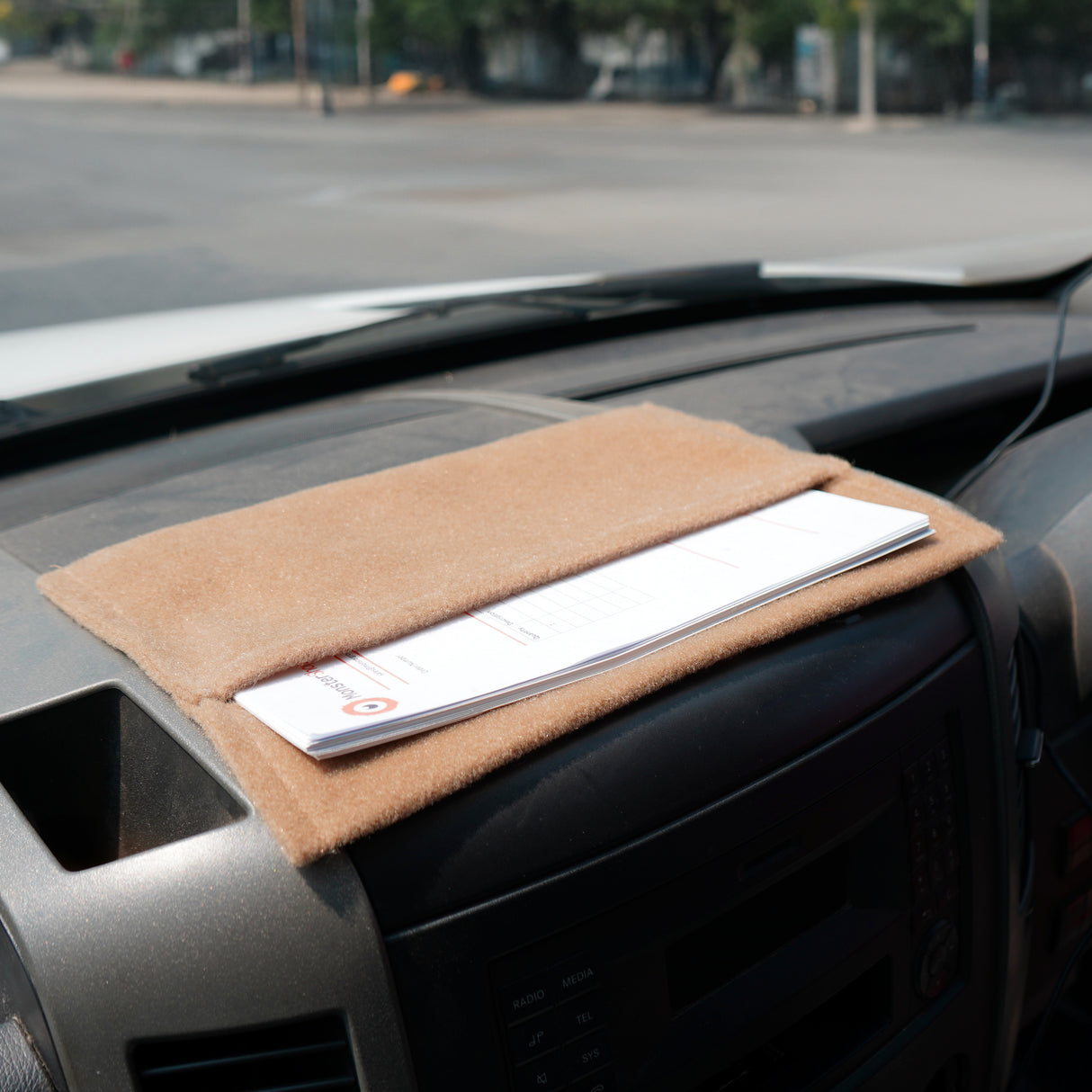 Poche de rangement beige en feutre, posée sur le tableau de bord d'une voiture, idéale pour organiser documents et petits objets