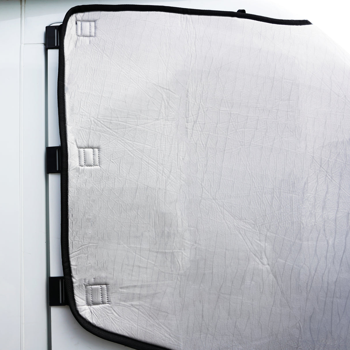 Couverture pare-soleil pour camping-car en matériau blanc texturé, avec des attaches noires, offrant une protection contre la chaleur et le soleil