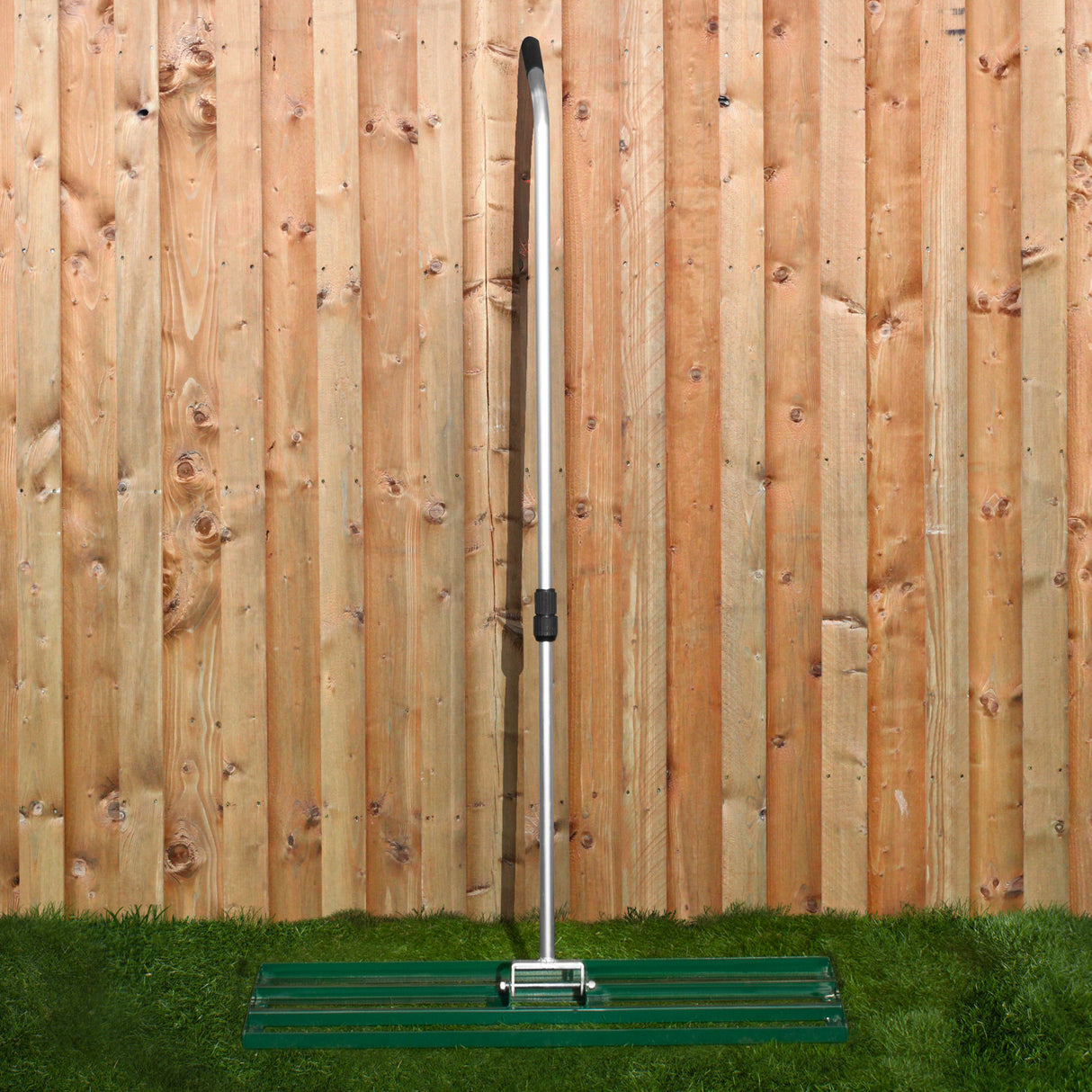 Ensemble scarificateur et niveleur de pelouse de 100 cm, avec une structure en métal argenté et un plateau vert, sur fond de clôture en bois