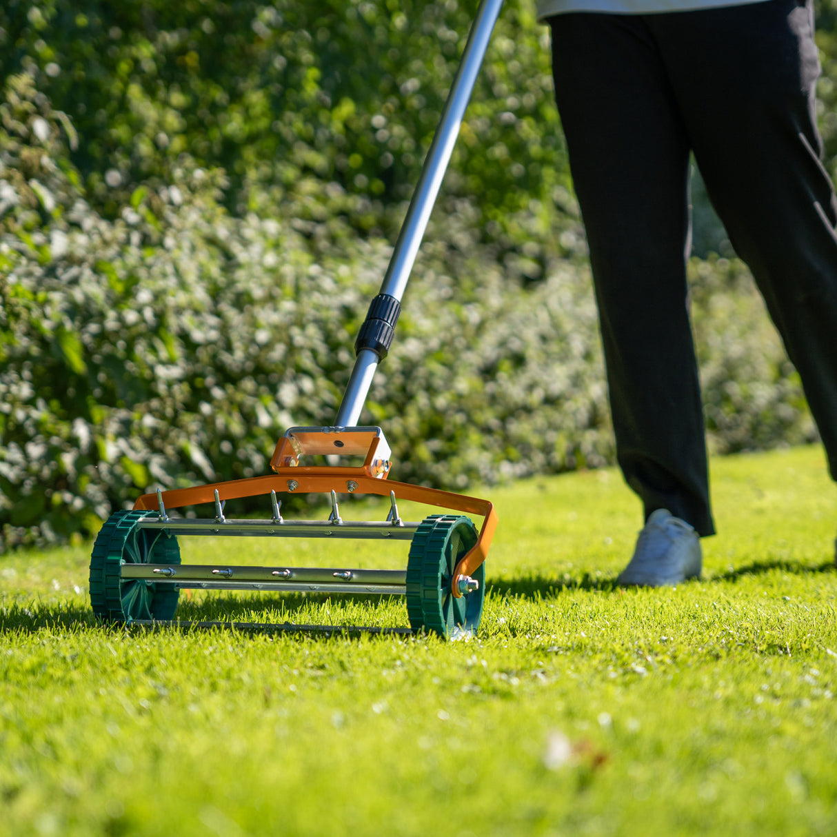 Scarificateur et niveleur de pelouse vert de 100 cm, avec rouleaux en métal et poignées ergonomiques, sur une pelouse bien entretenue