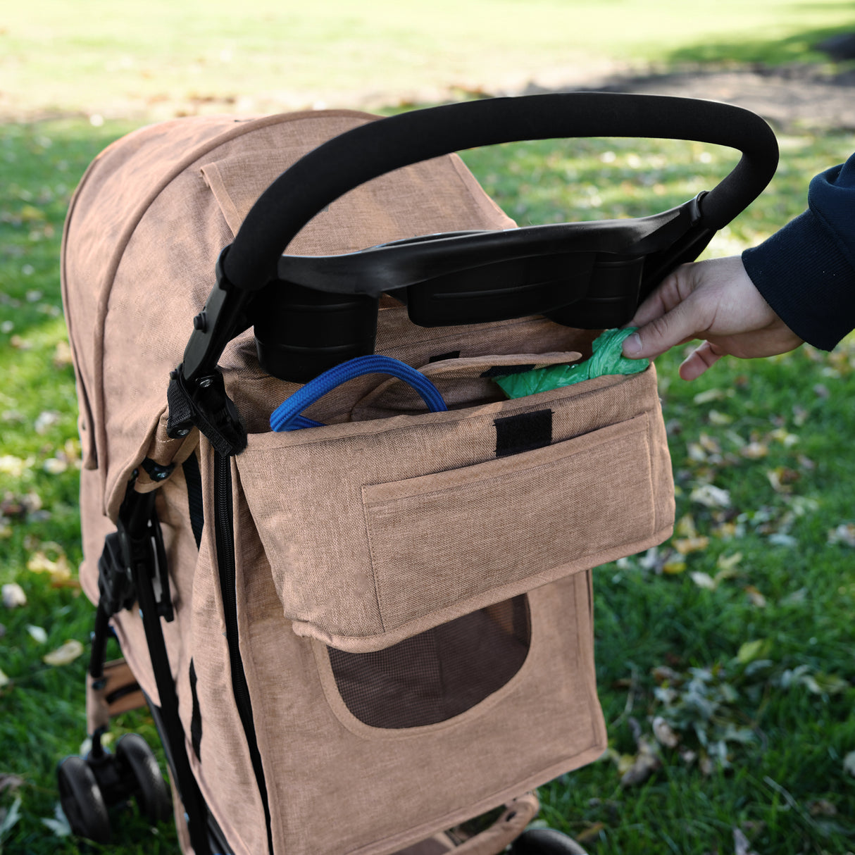 Sac caddy beige pour poussette d'animal, en tissu texturé, avec poches pratiques pour accessoires, posé sur une pelouse verte