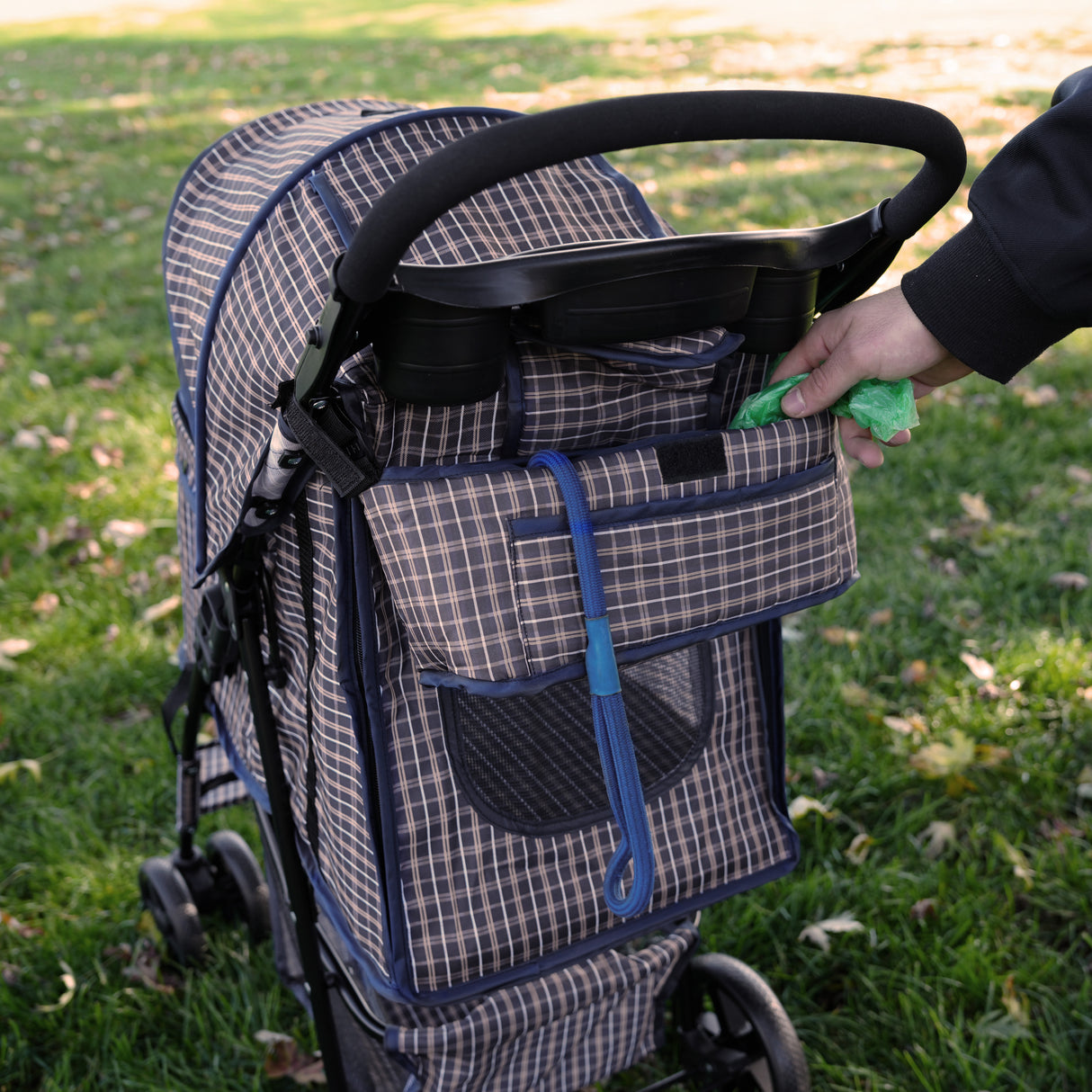 Poussette pour animal de compagnie en bleu tartan, avec un panier pratique, des poignées confortables et un design élégant sur fond de gazon vert