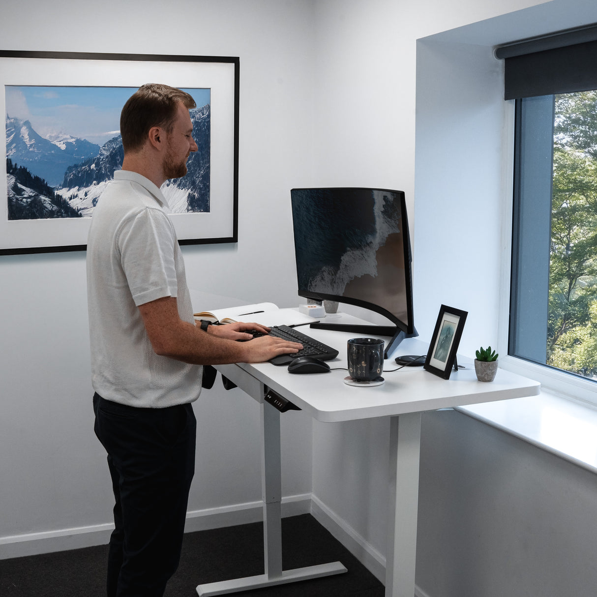 Bureau assis-debout électrique blanc avec tiroir, écran incurvé, clavier et plante sur un bureau moderne dans un bureau lumineux