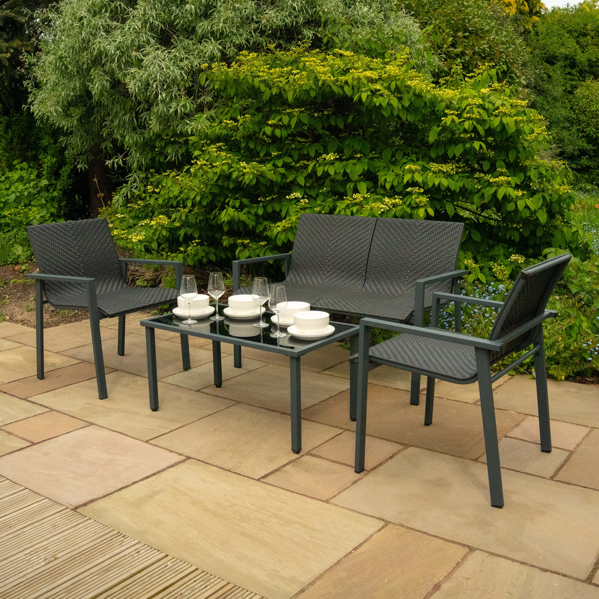 Ensemble de salon de terrasse en rotin noir, comprenant deux fauteuils, un canapé et une table basse, sur une terrasse en pierre