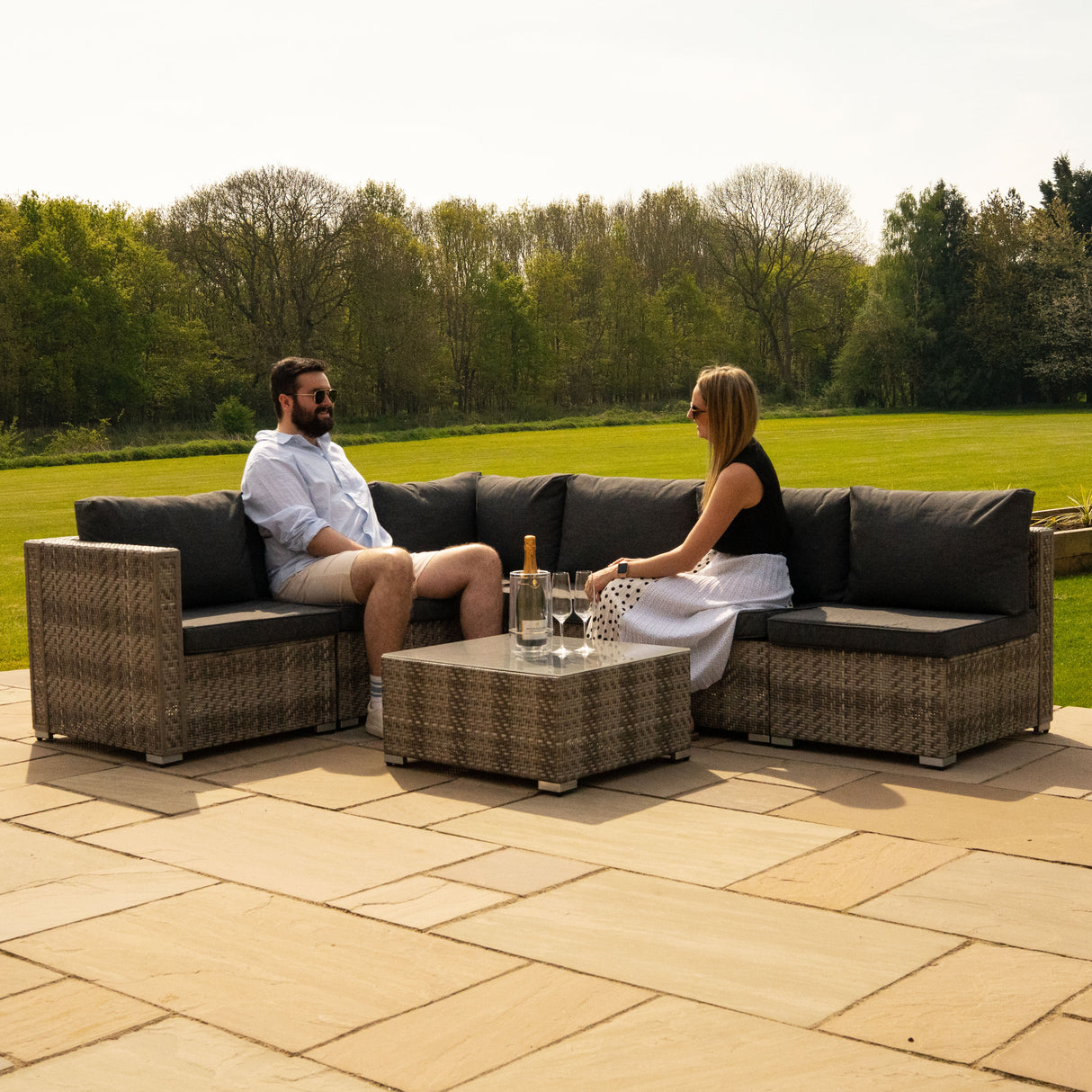 Salon de jardin modulaire en rotin gris avec coussins noirs, composé de canapés et d'une table basse, idéal pour l'extérieur