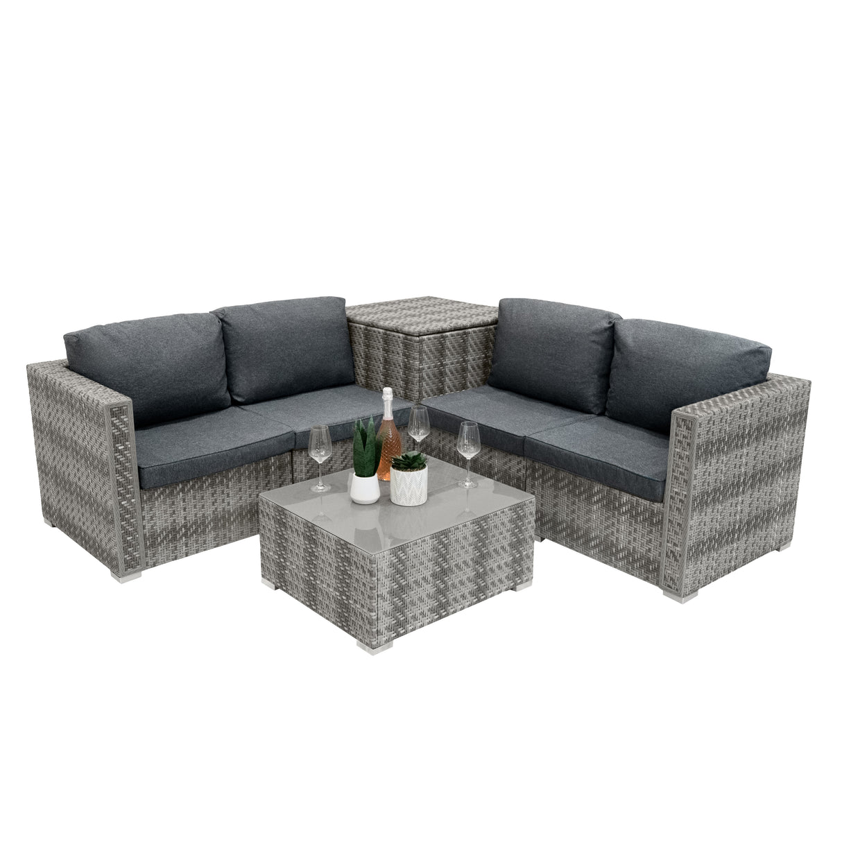 Salon de jardin modulaire en rotin gris, coussins gris foncé, table basse en verre, décoré avec des plantes et des verres élégants