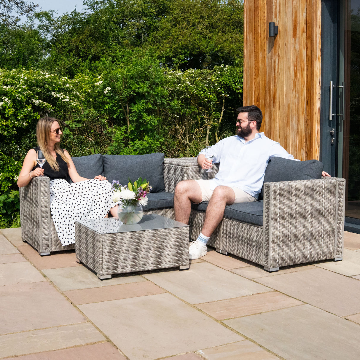 Salon de jardin modulaire en rotin gris, comprenant un canapé et une table basse, avec coussins gris, sur une terrasse ensoleillée