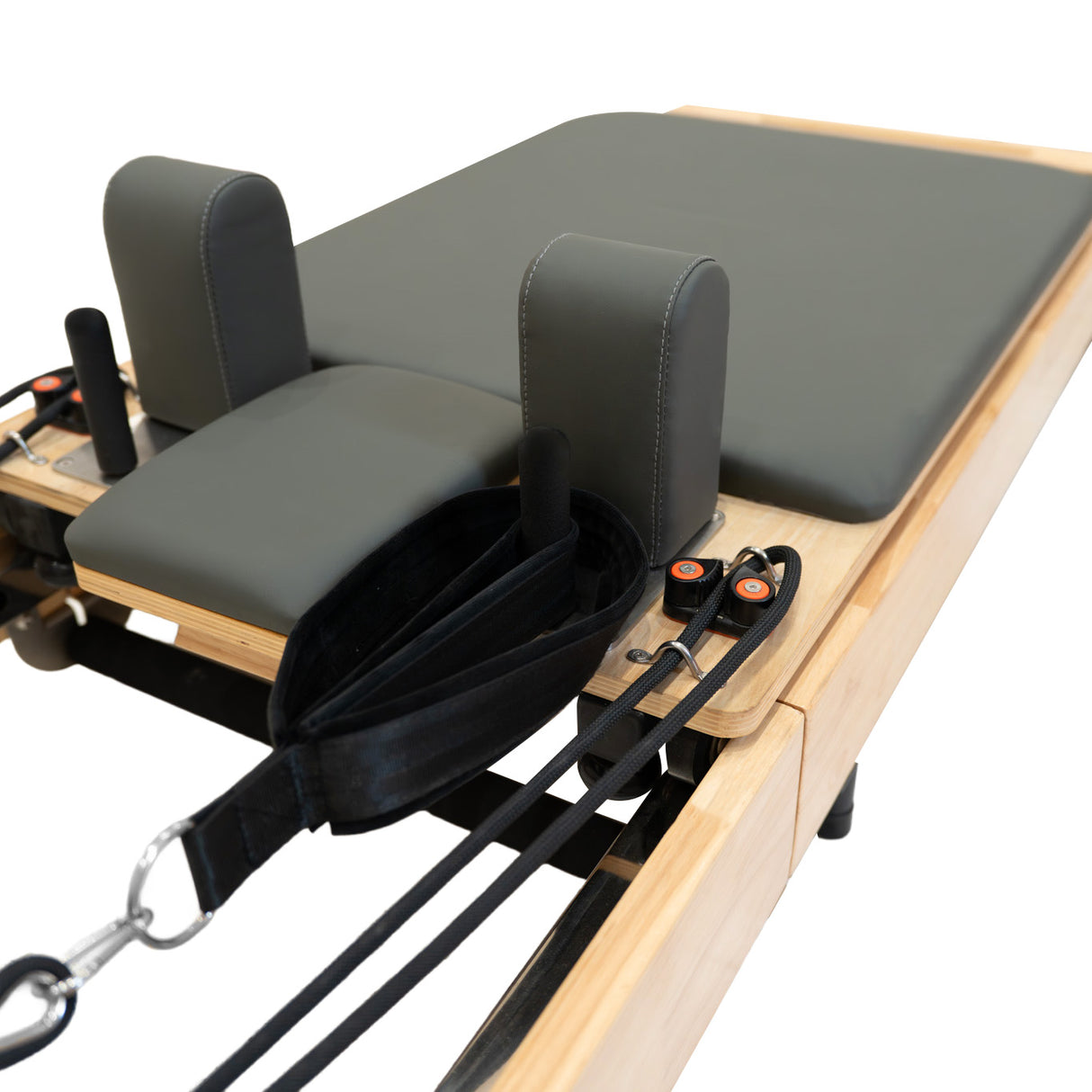 Machine reformer Pilates pliable en chêne, avec un coussin gris foncé, poignées noires et sangles ajustables pour un entraînement confortable