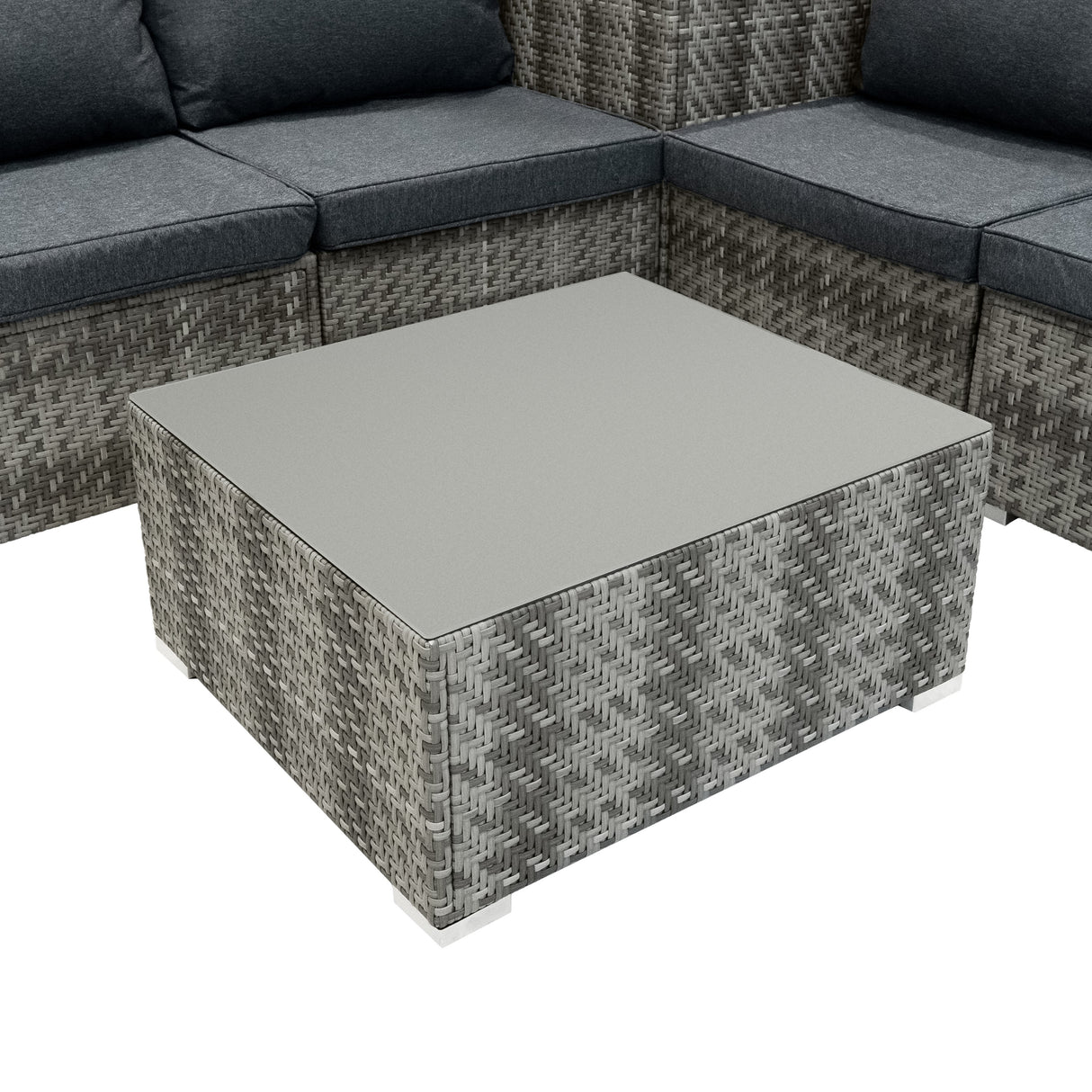 Table basse carrée en rotin gris avec plateau en verre, entourée de coussins gris sur un salon de jardin modulaire élégant