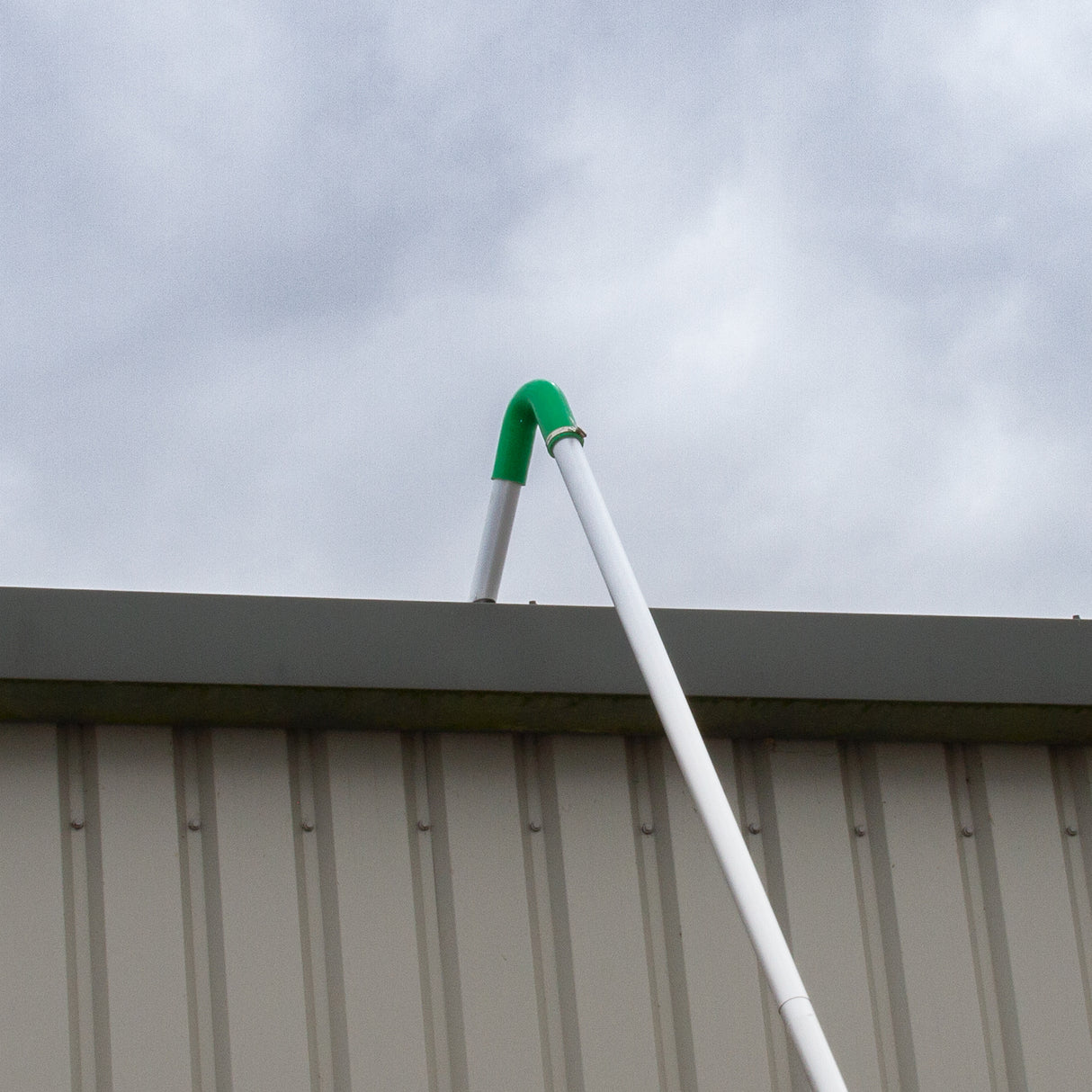 Perche de gouttière en plastique blanc avec embout vert, fixée sur le toit d'un bâtiment, idéale pour l'aspiration industrielle