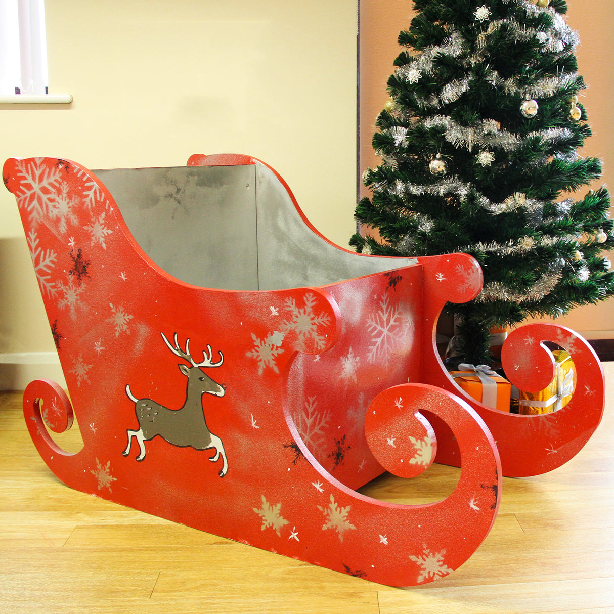 Traîneau du Père Noël en MDF naturel, rouge avec motifs de flocons de neige et un renne, décoré près d'un sapin de Noël