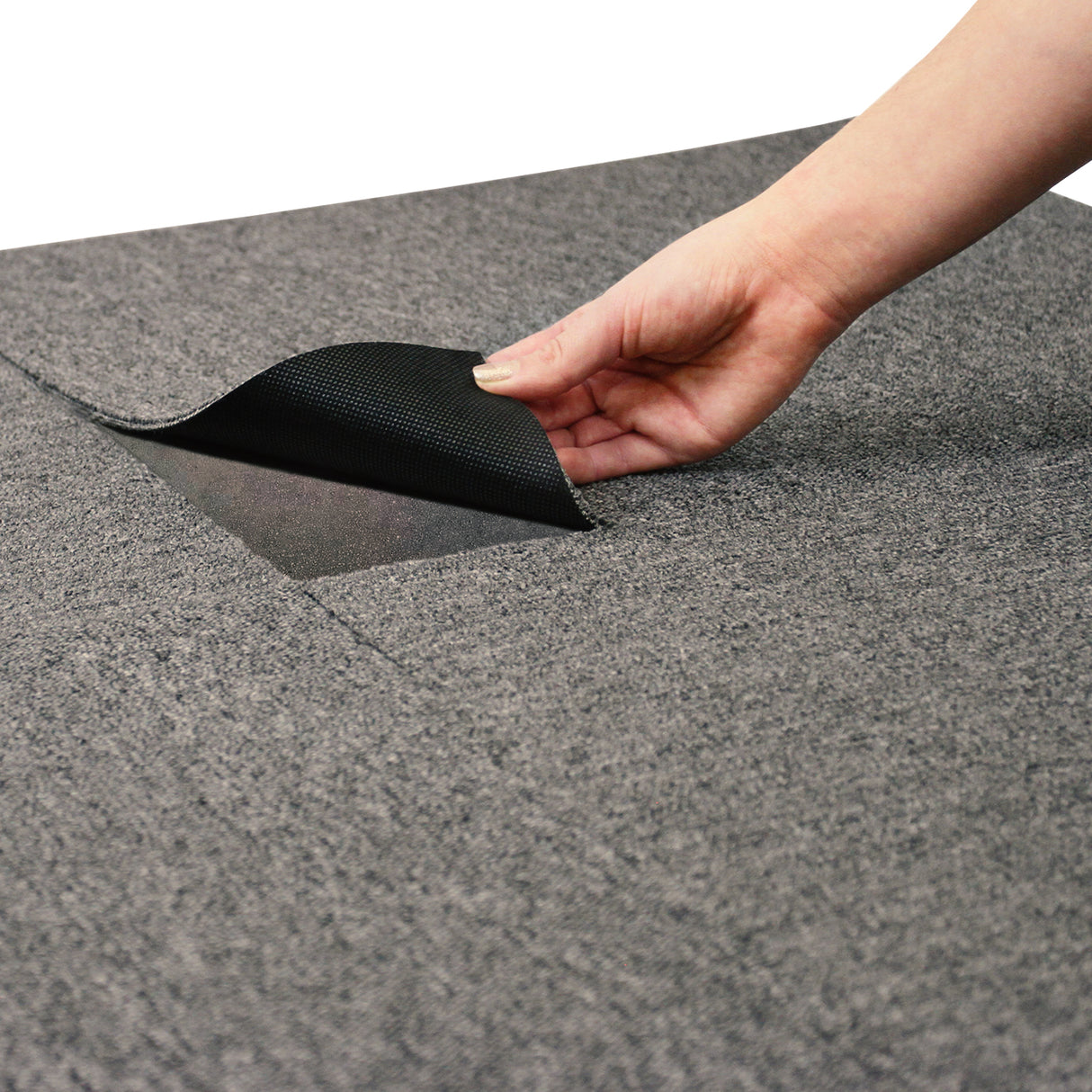 Dalle de moquette gris anthracite de 50 cm x 50 cm, texture douce, main soulevant un coin pour montrer la surface antidérapante en dessous