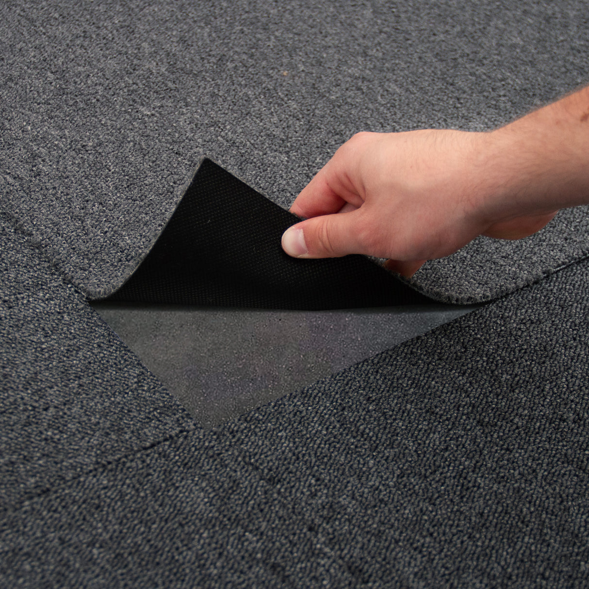 Dalles de moquette noir charbon de 50cm x 50cm, texture douce et résistante, montrant une main soulevant une dalle pour installation