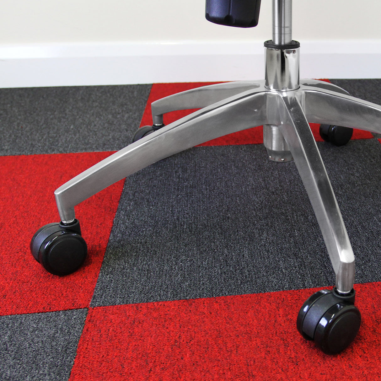 Dalles de moquette rouge écarlate de 50 cm x 50 cm, posées sur un sol gris, avec un fauteuil à roulettes en métal brillant