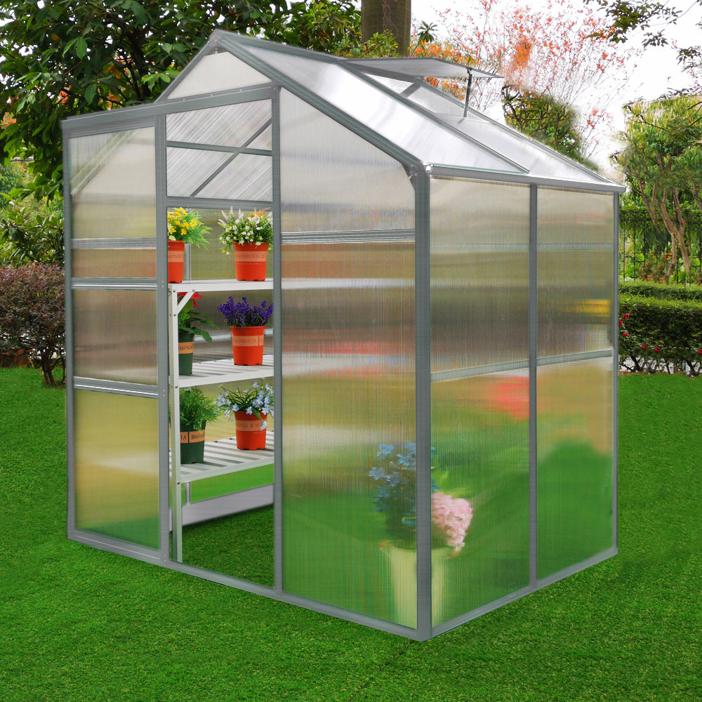 Serre de jardin en polycarbonate transparent, 1,8 m x 1,2 m, avec étagères blanches et pots de fleurs colorés sur un gazon vert