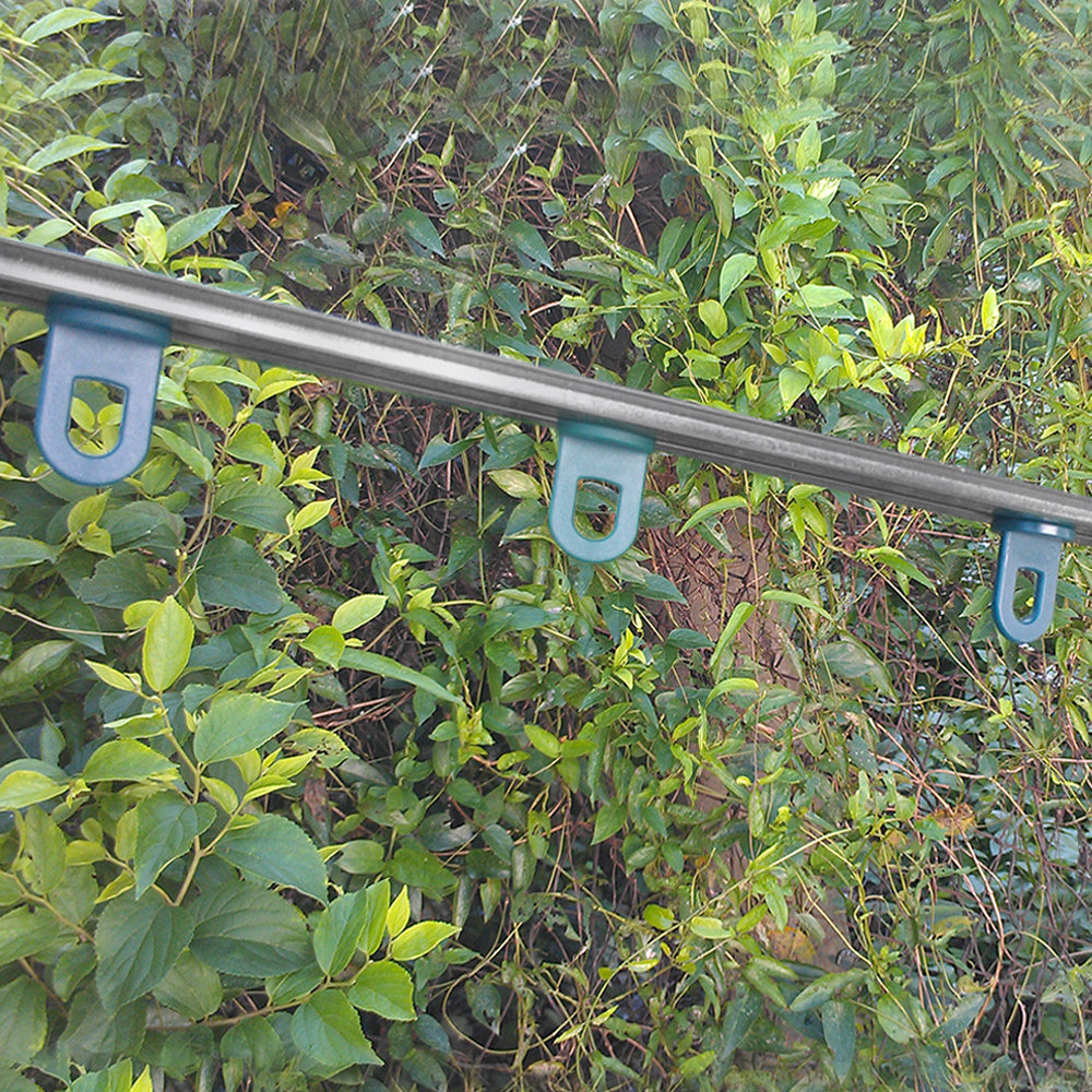 Barre en métal avec crochets bleus, fixée sur un fond de feuillage vert, idéale pour suspendre des plantes dans une serre de jardin