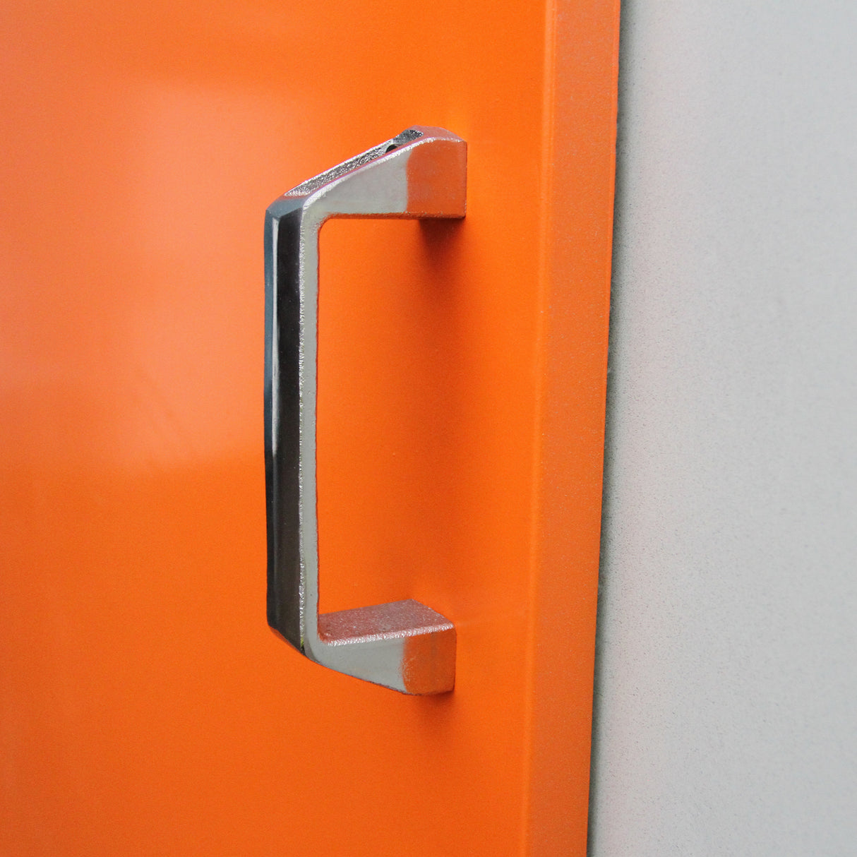 Poignée en métal chromé sur un four de séchage orange vif, avec une finition lisse et brillante, idéale pour le revêtement peinture