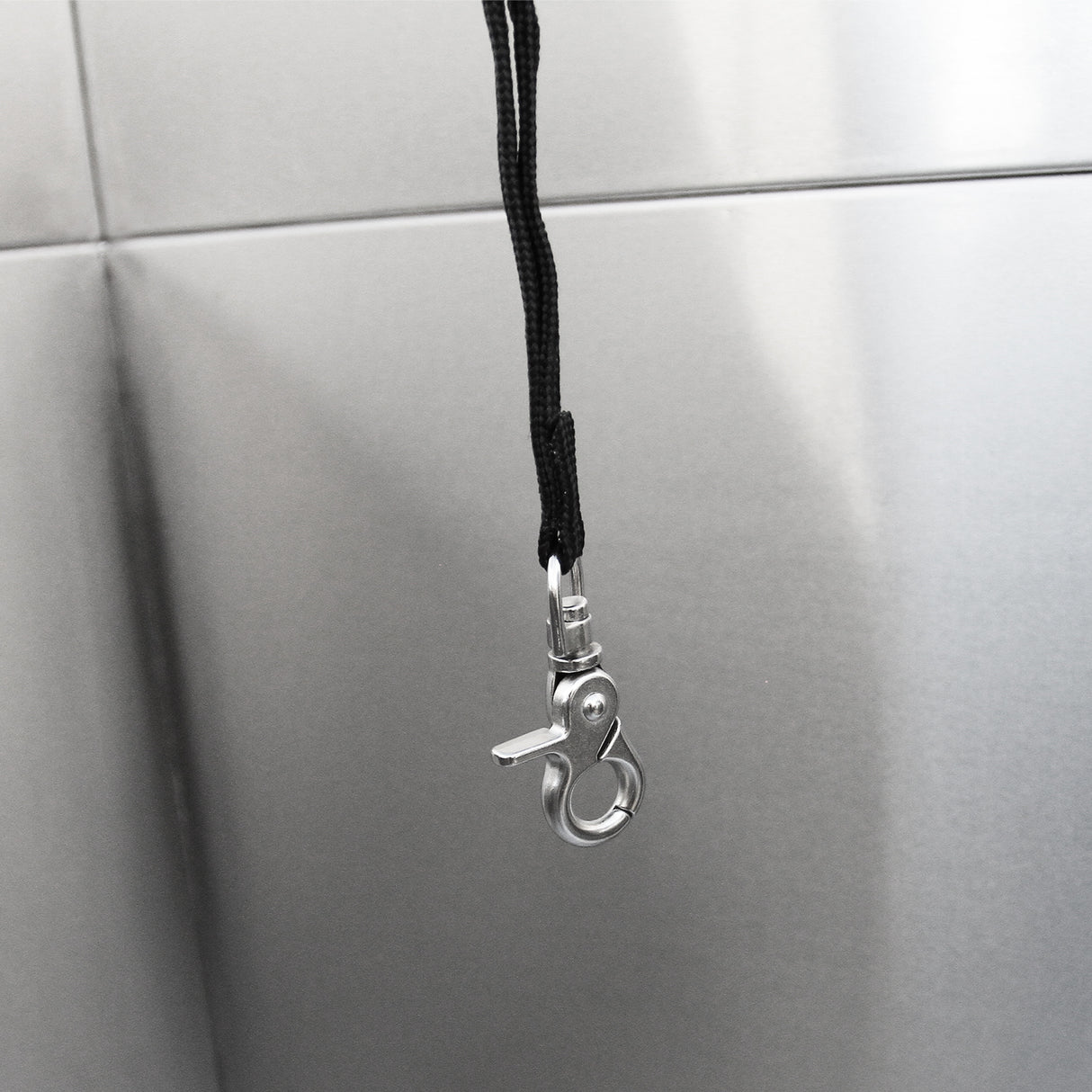 Crochet en métal brillant suspendu par une corde noire, avec un fond en inox lisse et réfléchissant, idéal pour la baignoire de toilettage